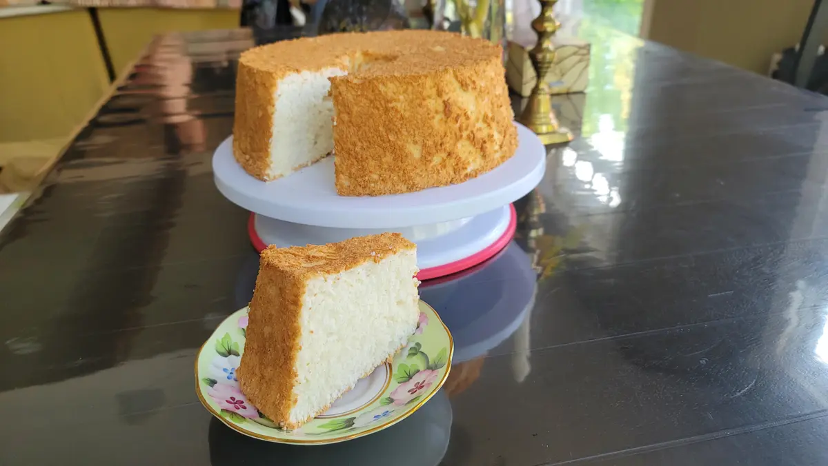 Tall fluffy angel food cake with light golden top, sliced to show airy white interior crumb structure