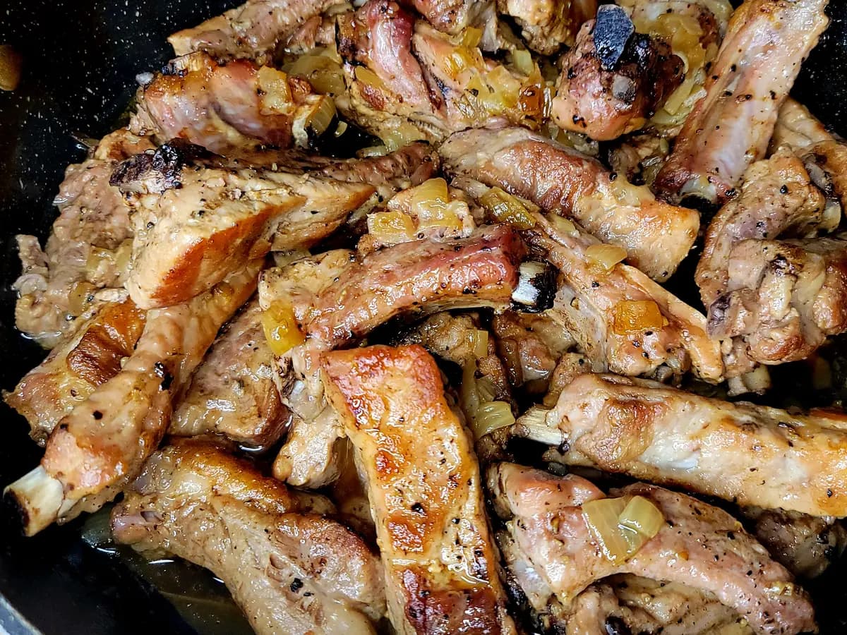 Tender braised pork ribs glistening with savory sauce in a white ceramic dish, garnished with bay leaves