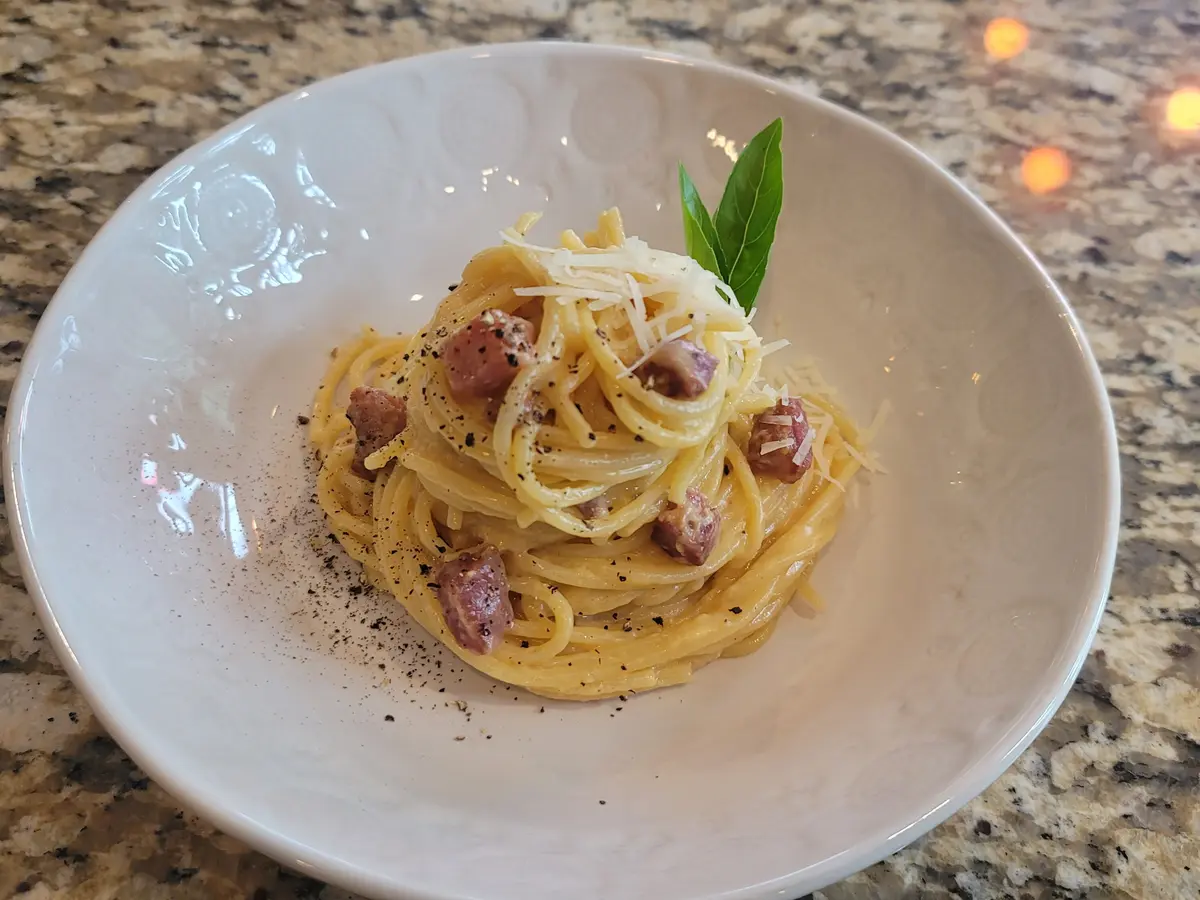 Creamy carbonara pasta with crispy guanciale, fresh cracked pepper, and grated Pecorino Romano on a white plate