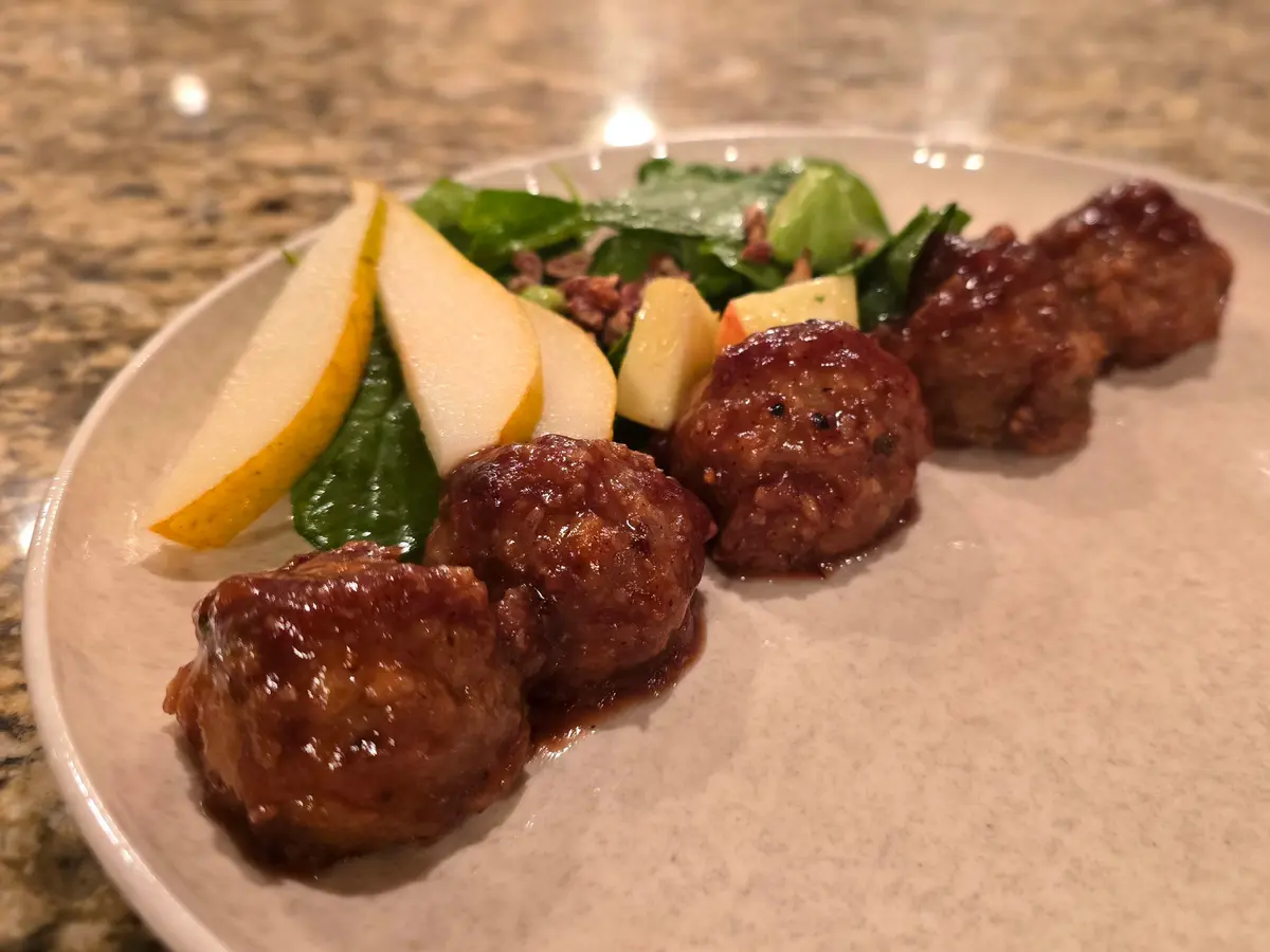 Golden-brown turkey meatballs coated in glossy cranberry glaze on a white plate with fresh herb garnish