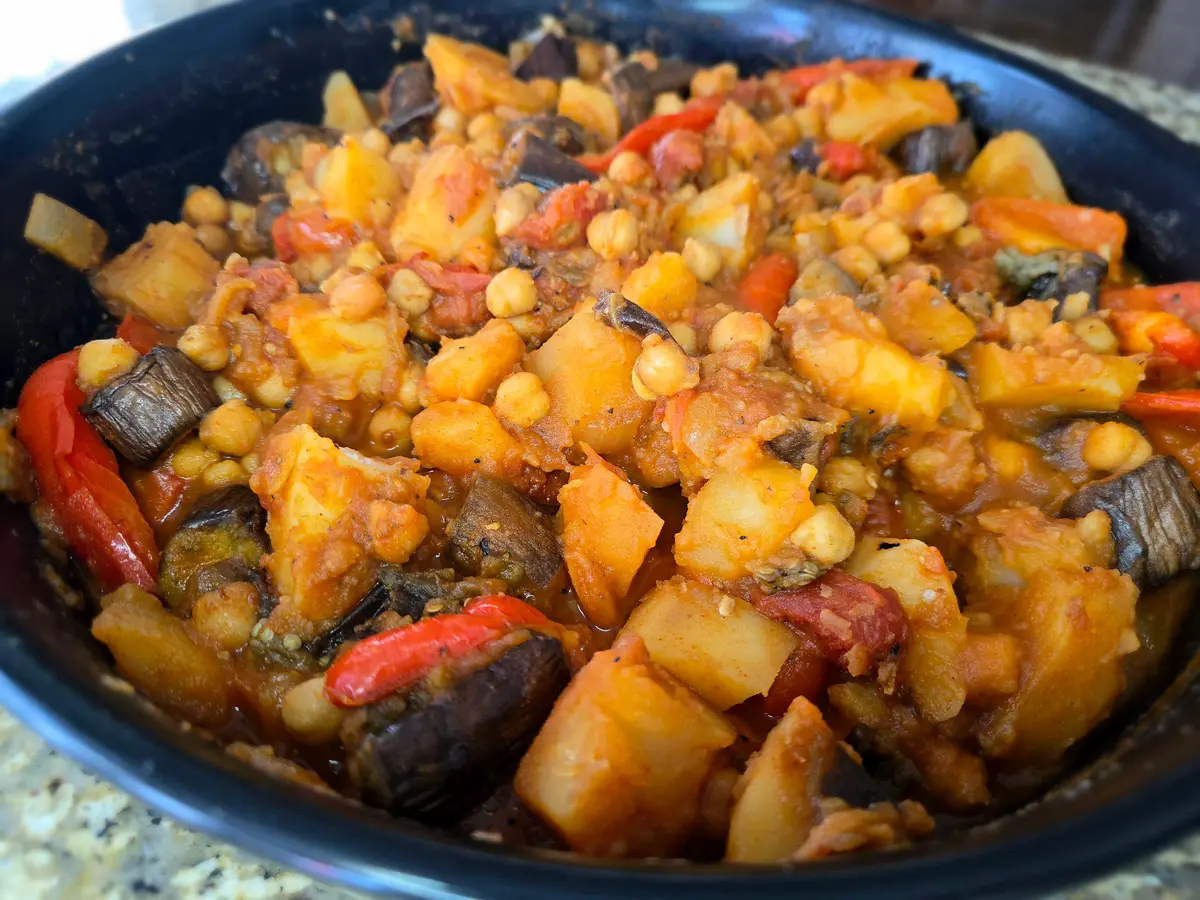 Steaming bowl of potato eggplant stew with red bell peppers, chickpeas, and fresh tomatoes in warm broth