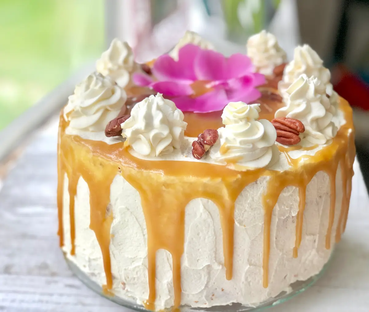 Golden-brown Shmoo cake with thick whipped cream frosting and caramel sauce drizzle on a white plate.
