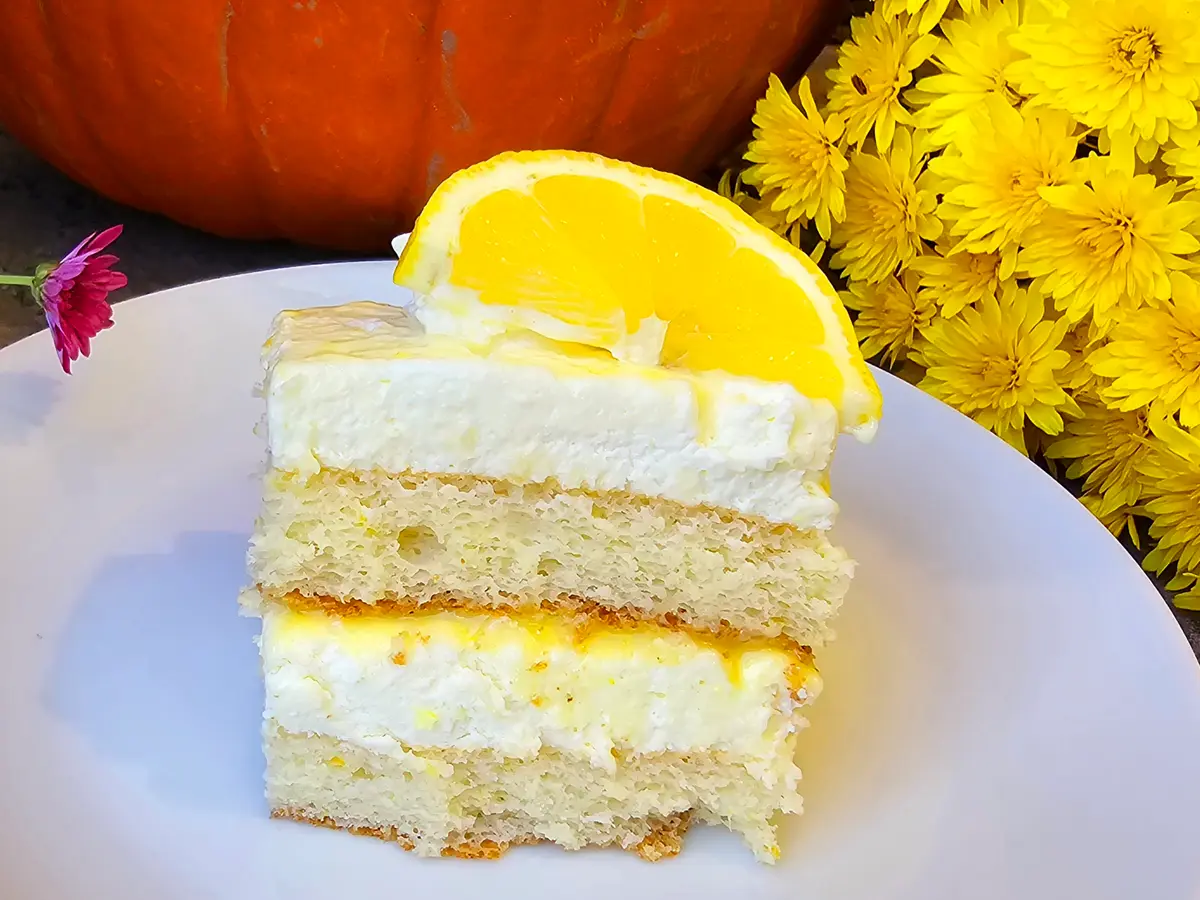 Creamy lemon mousse cake with mascarpone topping, garnished with fresh lemon zest on a white plate
