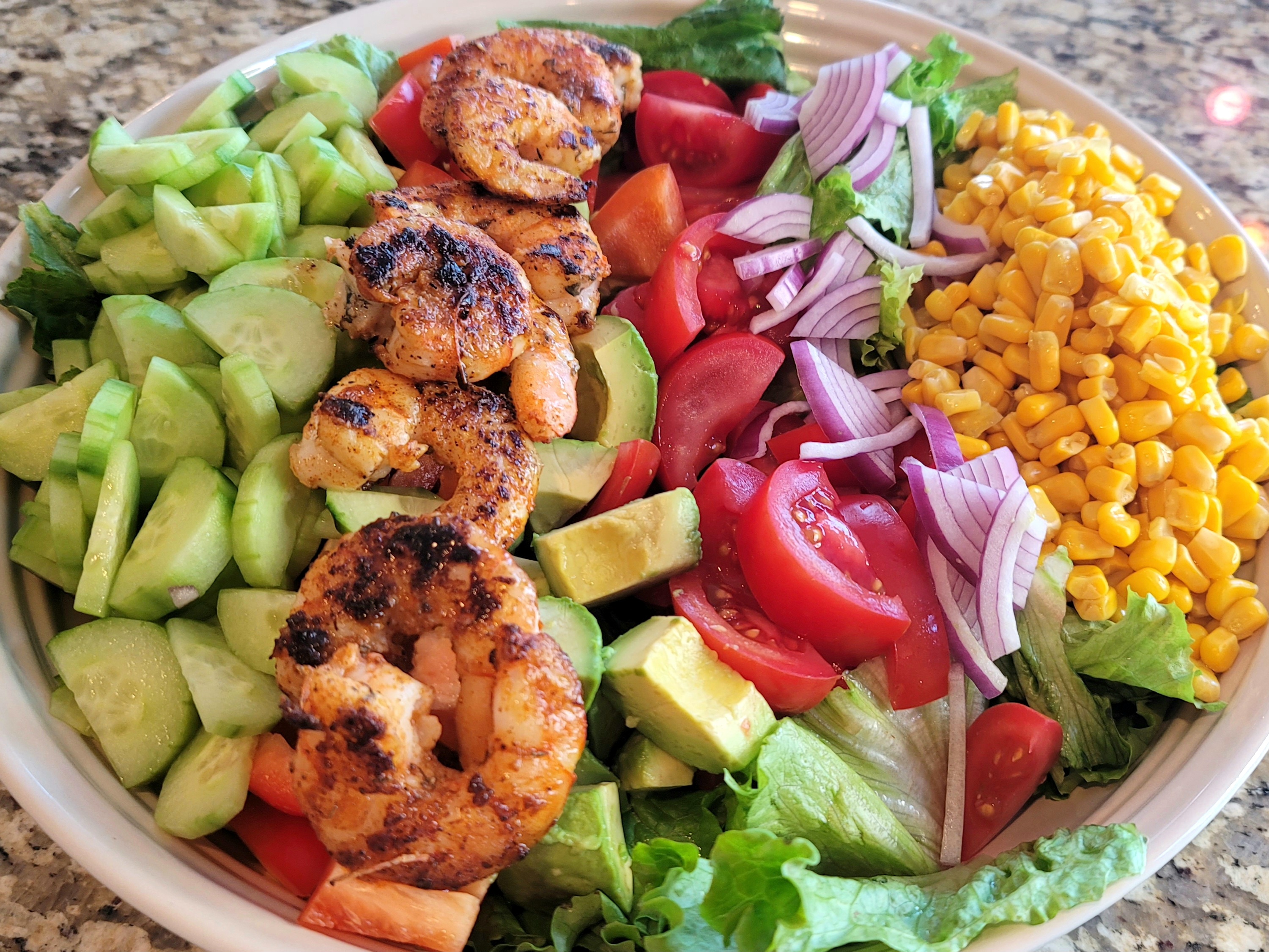 Colorful avocado corn salad with Cajun shrimp, romaine lettuce, tomatoes, cucumber, and fresh lime dressing in a white bowl