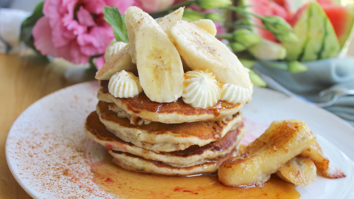 Stack of golden fluffy banana pancakes topped with butter and syrup on a white plate