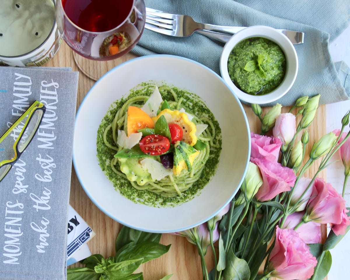 Bright green basil pesto pasta with fresh basil leaves, parmesan cheese, and pine nuts on a white plate