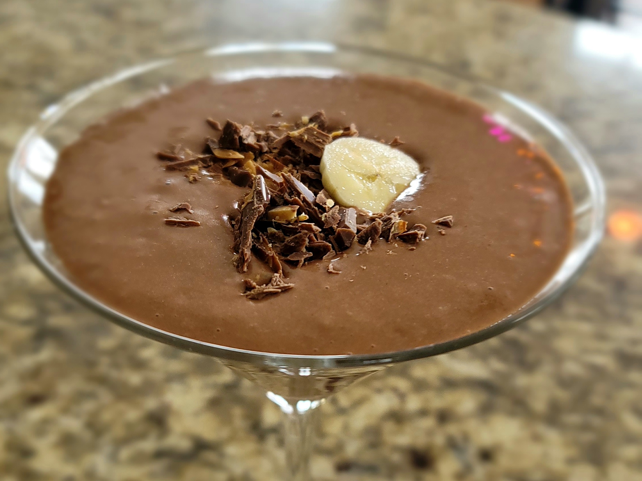 Chocolate peanut butter banana smoothie in a tall glass topped with sliced bananas and chocolate shavings
