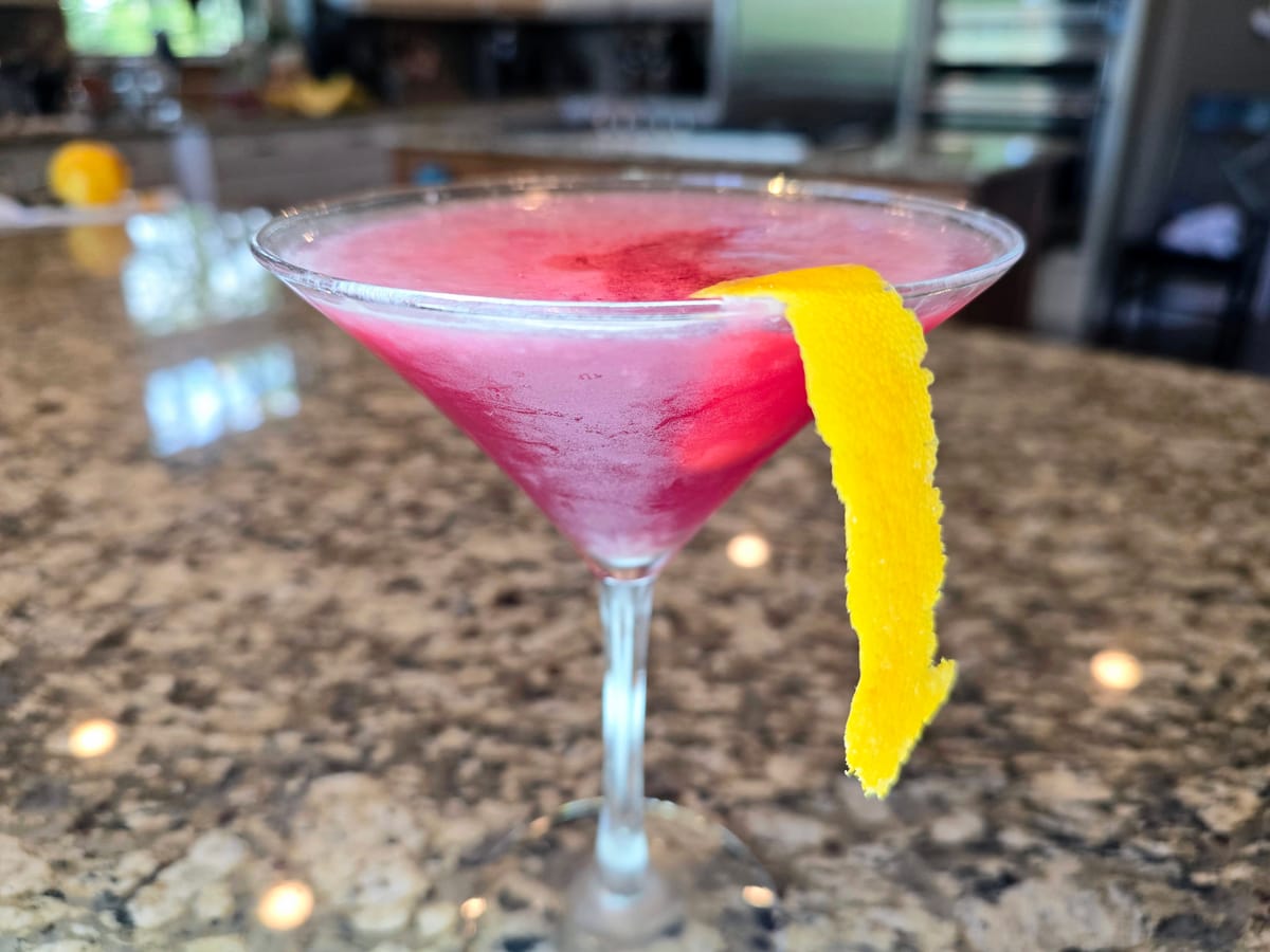 Cosmopolitan cocktail in a coupe glass with cranberry-pink color and orange spiral garnish