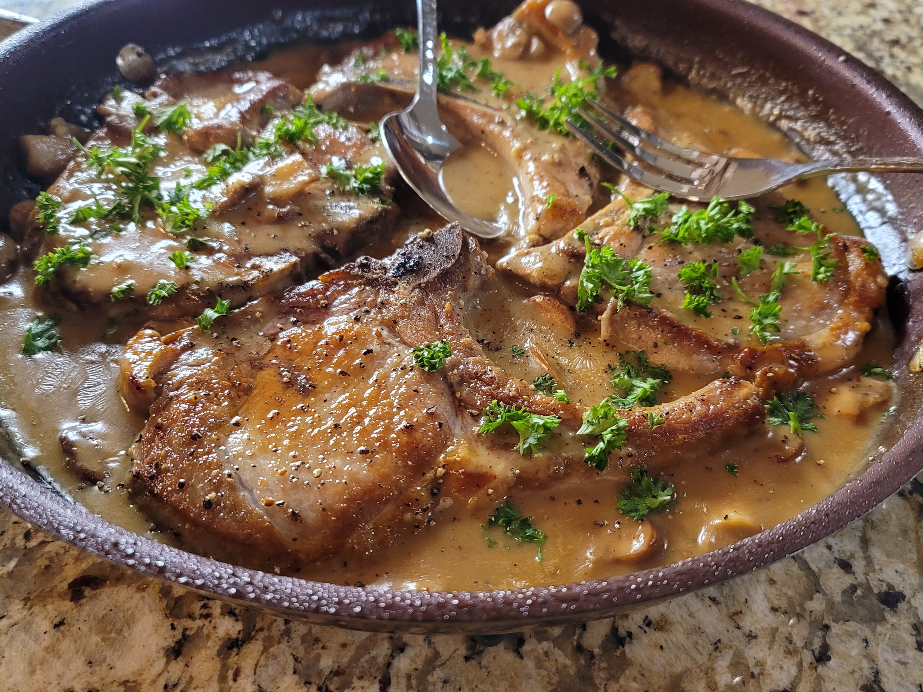 Creamy garlicky pork chops with mushrooms on a white plate with rich sauce and fresh herbs