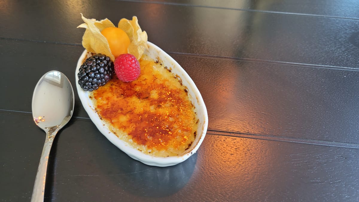 Silky crème brûlée with caramelized sugar crust and vanilla bean specks in white ramekin