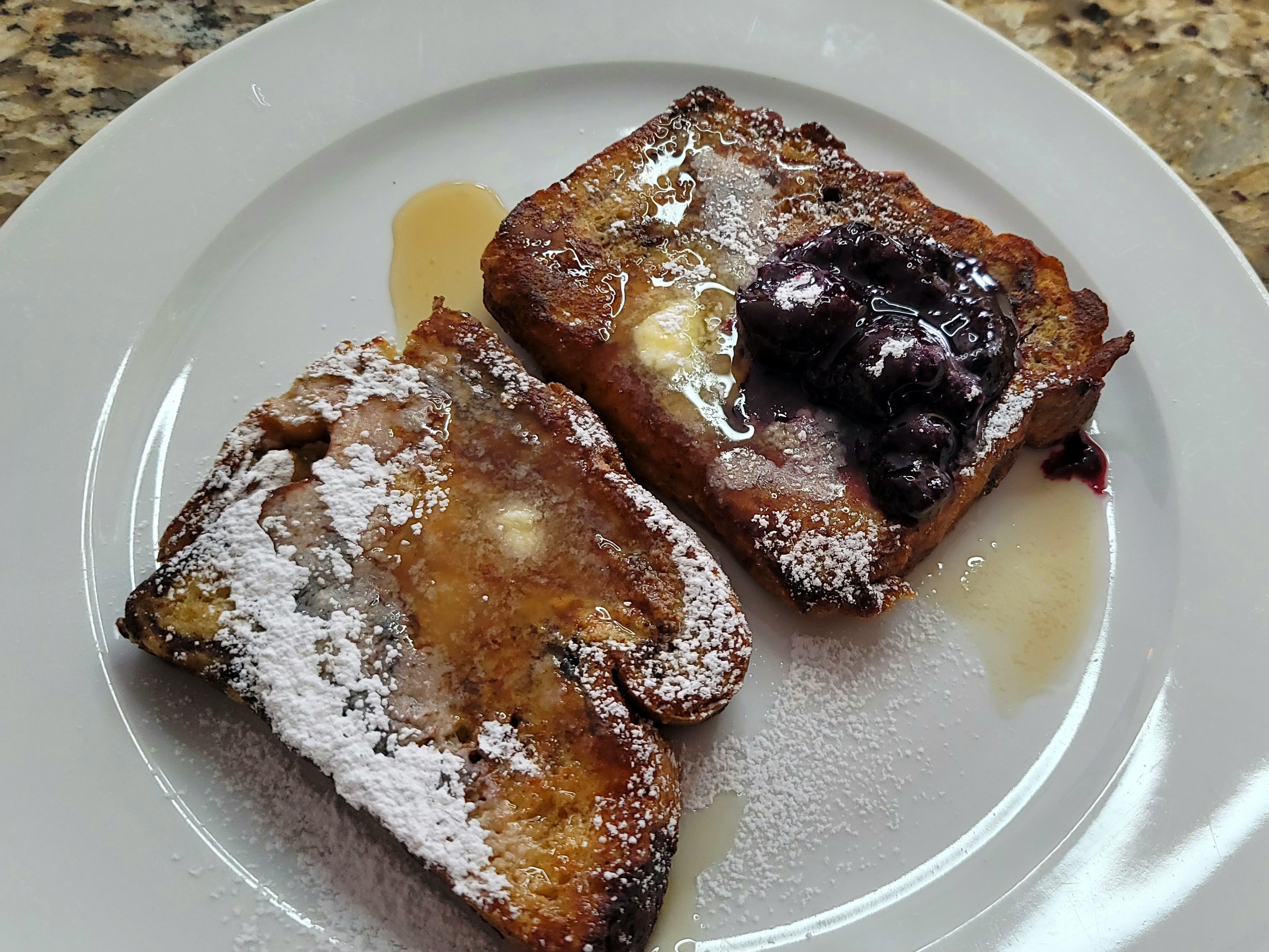 Golden crispy French toast slices stacked on a plate with maple syrup, powdered sugar, and fresh berries