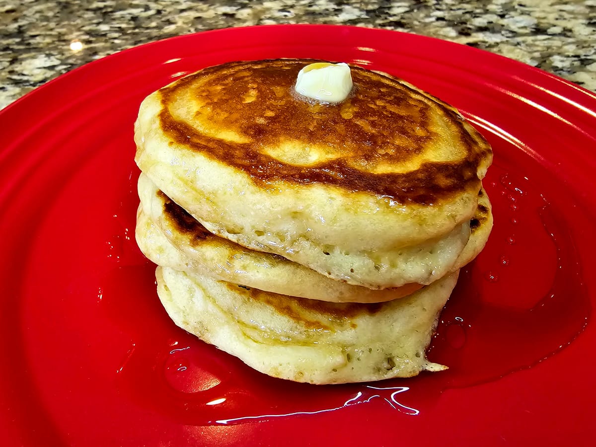Stack of golden fluffy pancakes with melting butter and syrup on a white plate