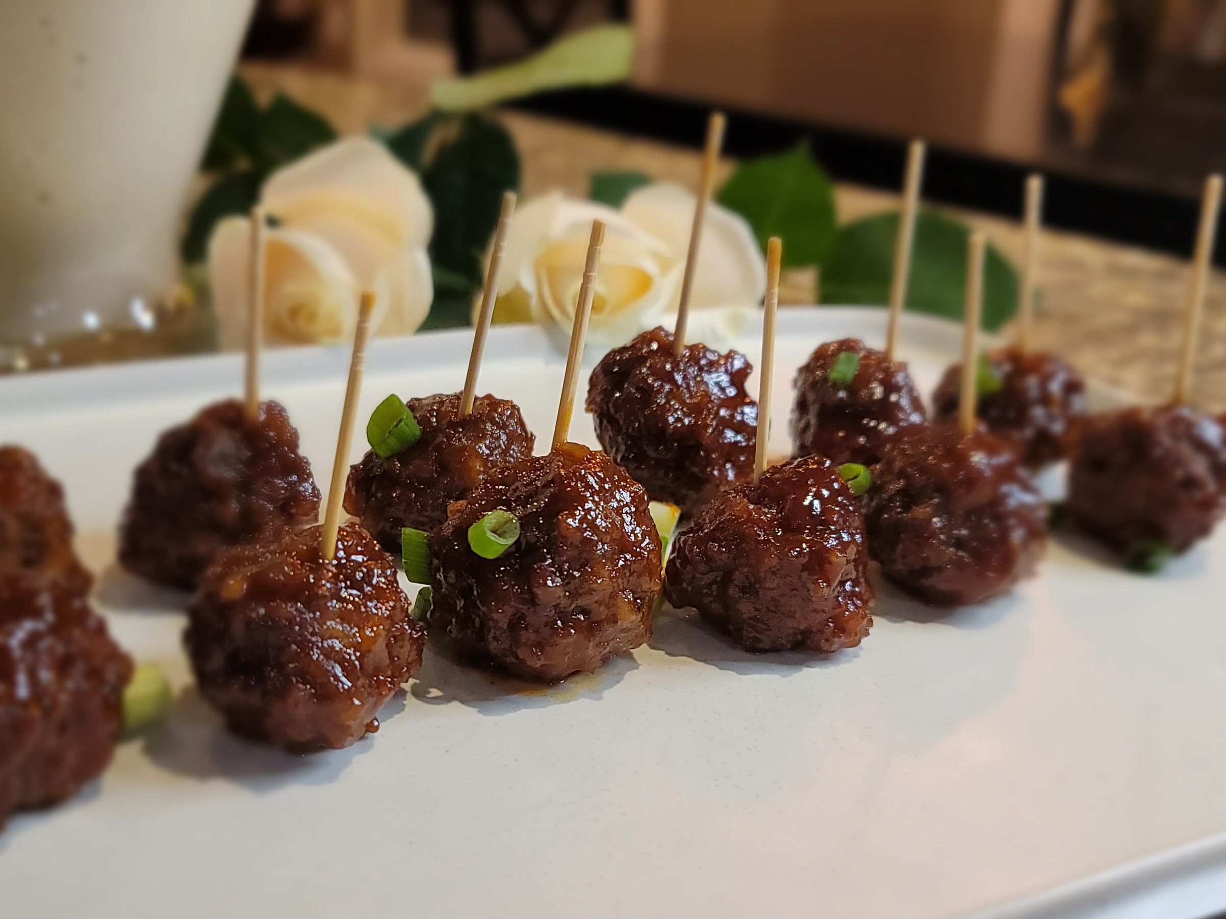 Glazed grape jelly meatballs in a white dish with glossy sauce and fresh herbs garnish