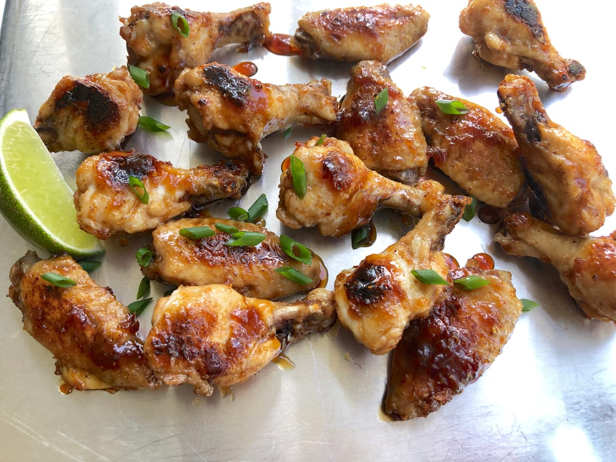 Golden crispy honey garlic chicken wings glazed with caramelized sauce on a white plate with sesame seeds and green onions