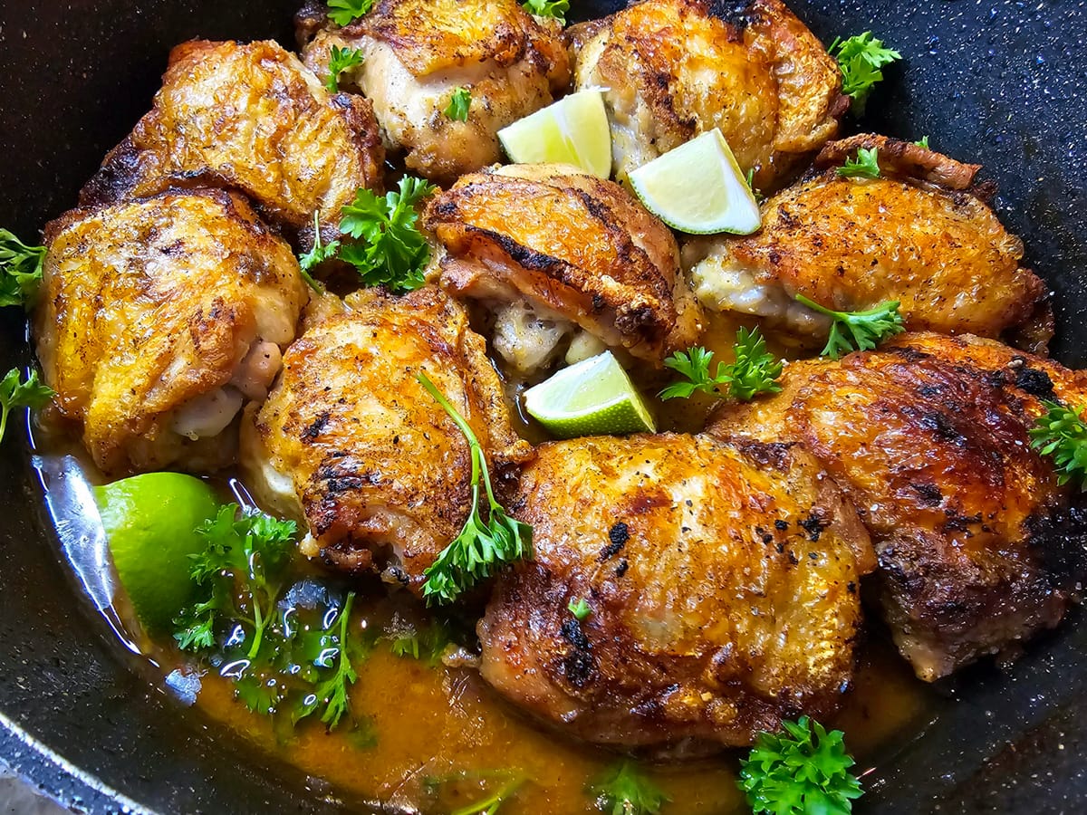 Golden brown honey lime chicken thighs on a white plate garnished with fresh cilantro and lime wedges