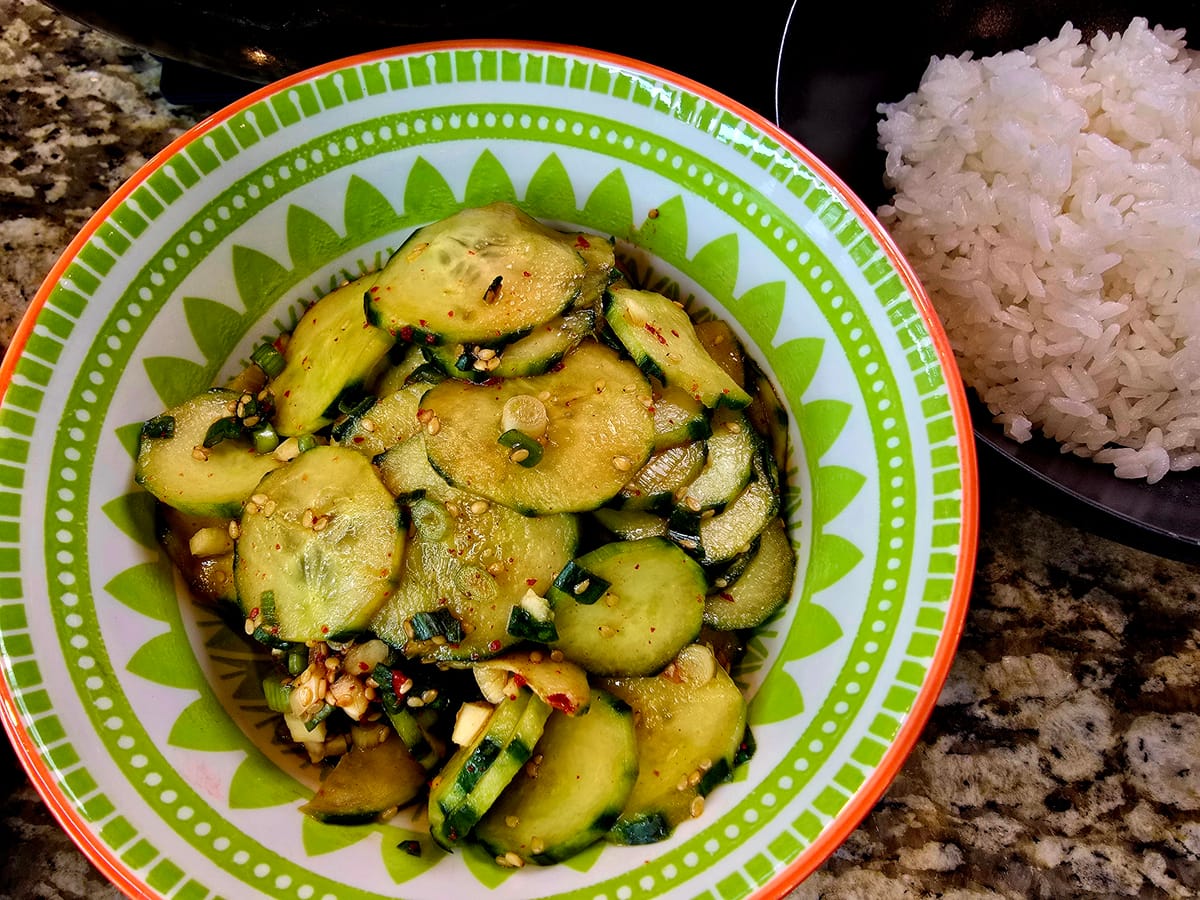 Korean spicy cucumber salad (oi muchim) with crispy sliced cucumbers, red gochugaru seasoning, sesame seeds, and green onion on a white plate