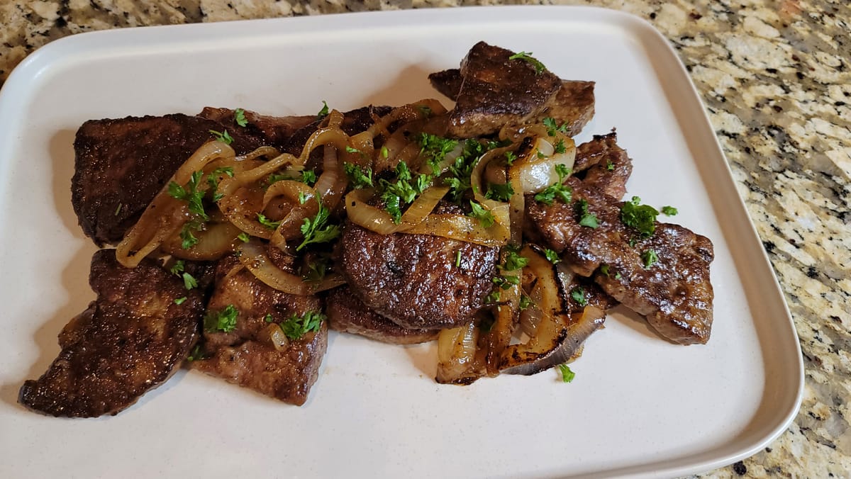 Pan-fried liver and onions on a white plate with golden caramelized onions and fresh herbs