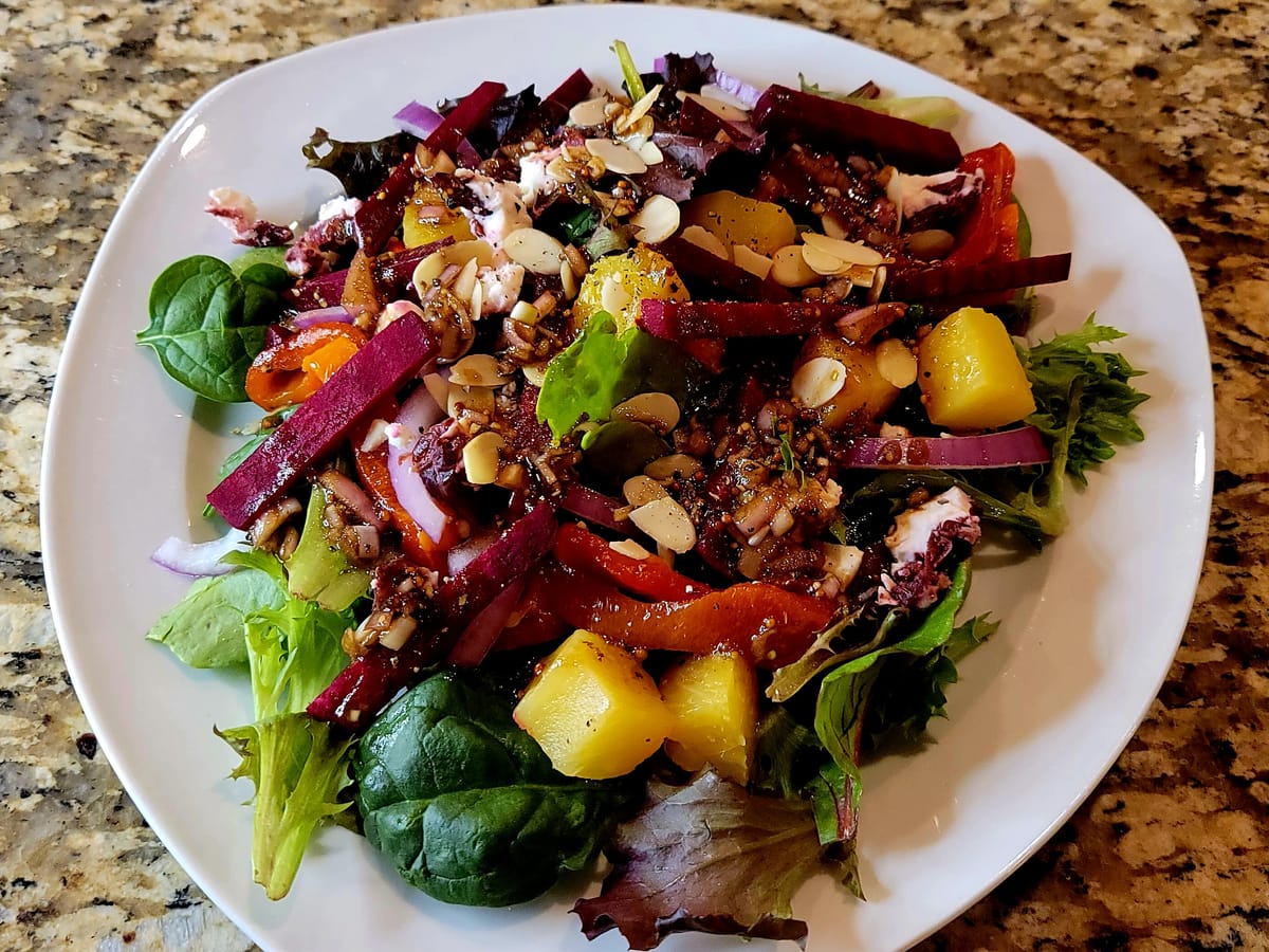 Colorful pineapple, beet and goat cheese salad on a white plate with mixed greens and creamy goat cheese crumbles