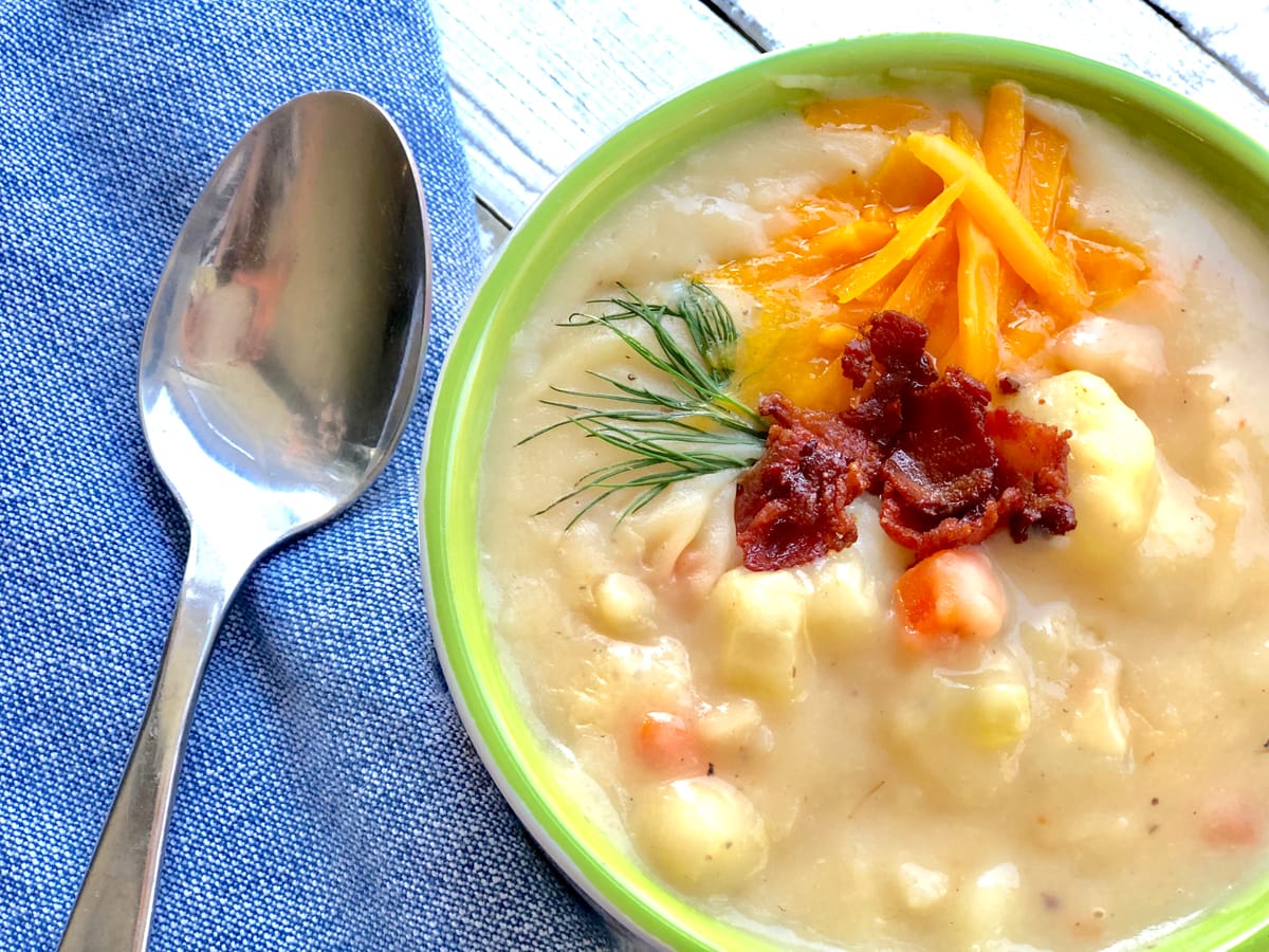 Creamy potato bacon soup with crispy bacon bits and fresh herbs in a white bowl on a rustic table