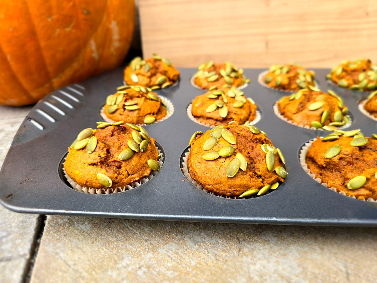 Golden-brown pumpkin muffins stacked on a plate with warm autumn spices and fresh pumpkin puree