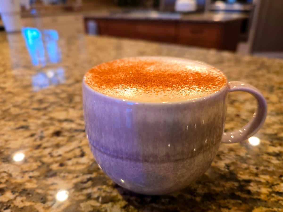 Barista-style pumpkin spice latte in a white cup with whipped cream and cinnamon on top, steaming hot