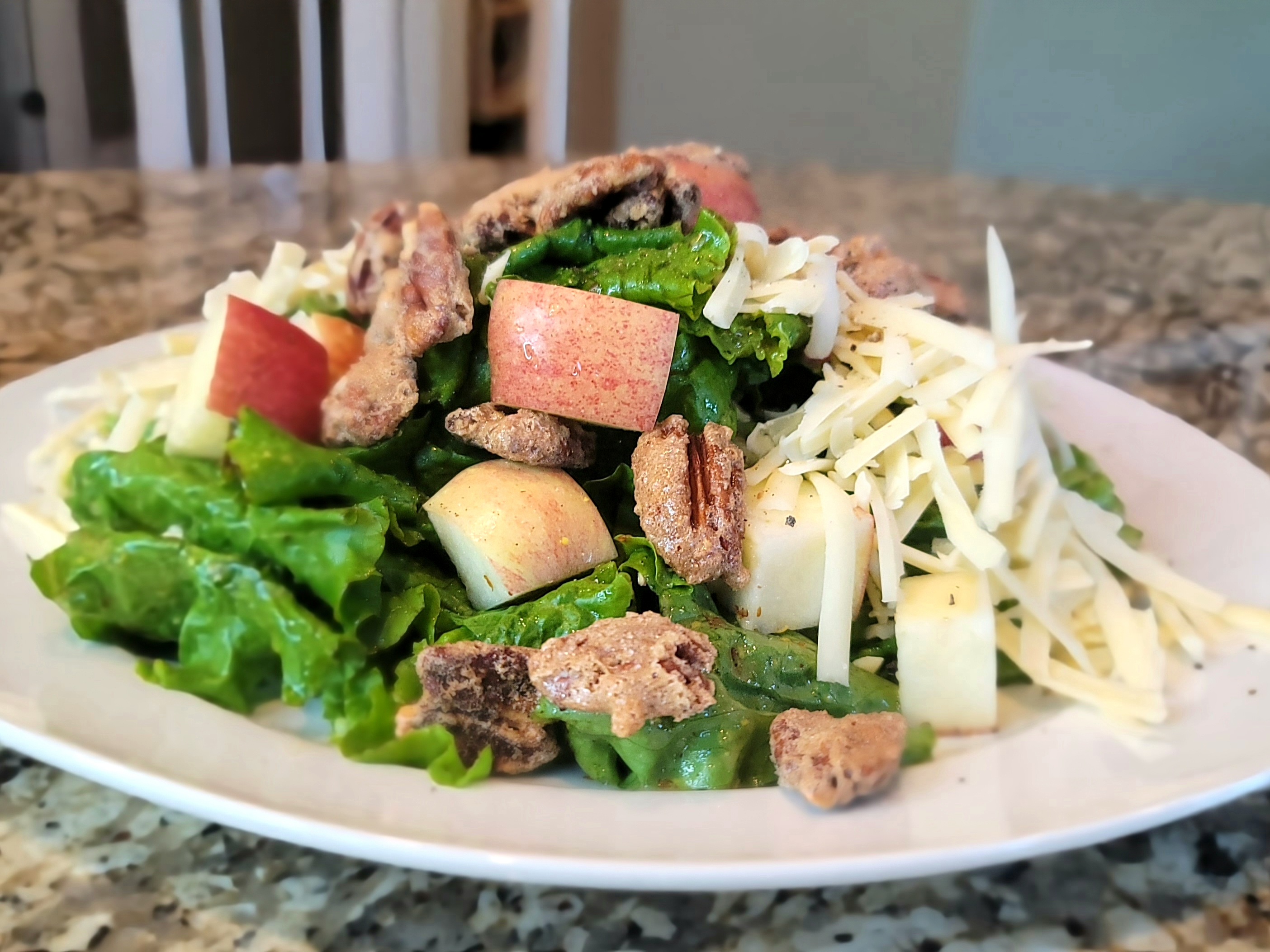 Rustic Retreat Salad with fresh green leaves, sliced apples, candied pecans, and smoked Gouda on a white plate