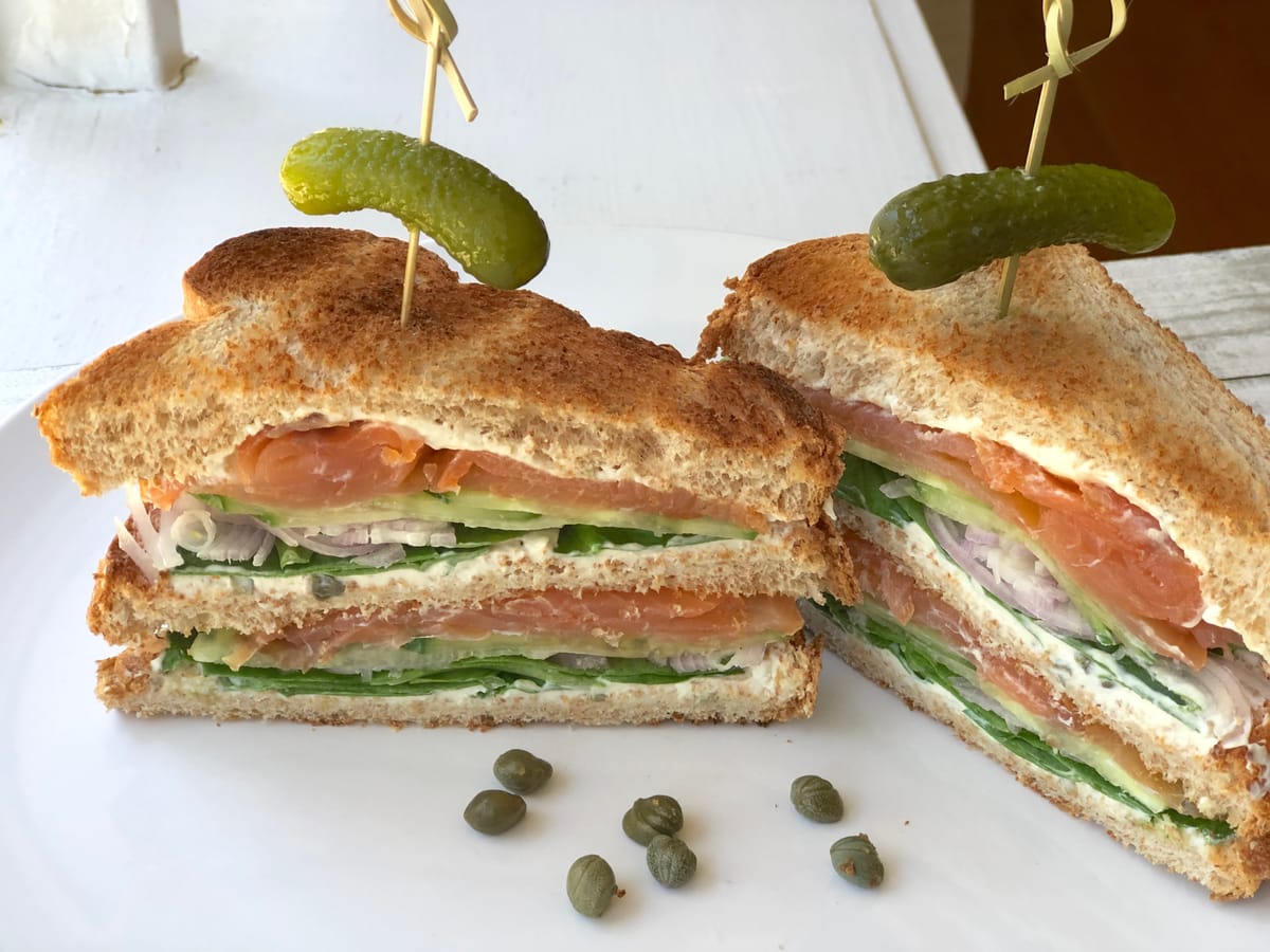 Gourmet smoked salmon sandwich with creamy spread, fresh dill, and crispy toasted bread on a white plate