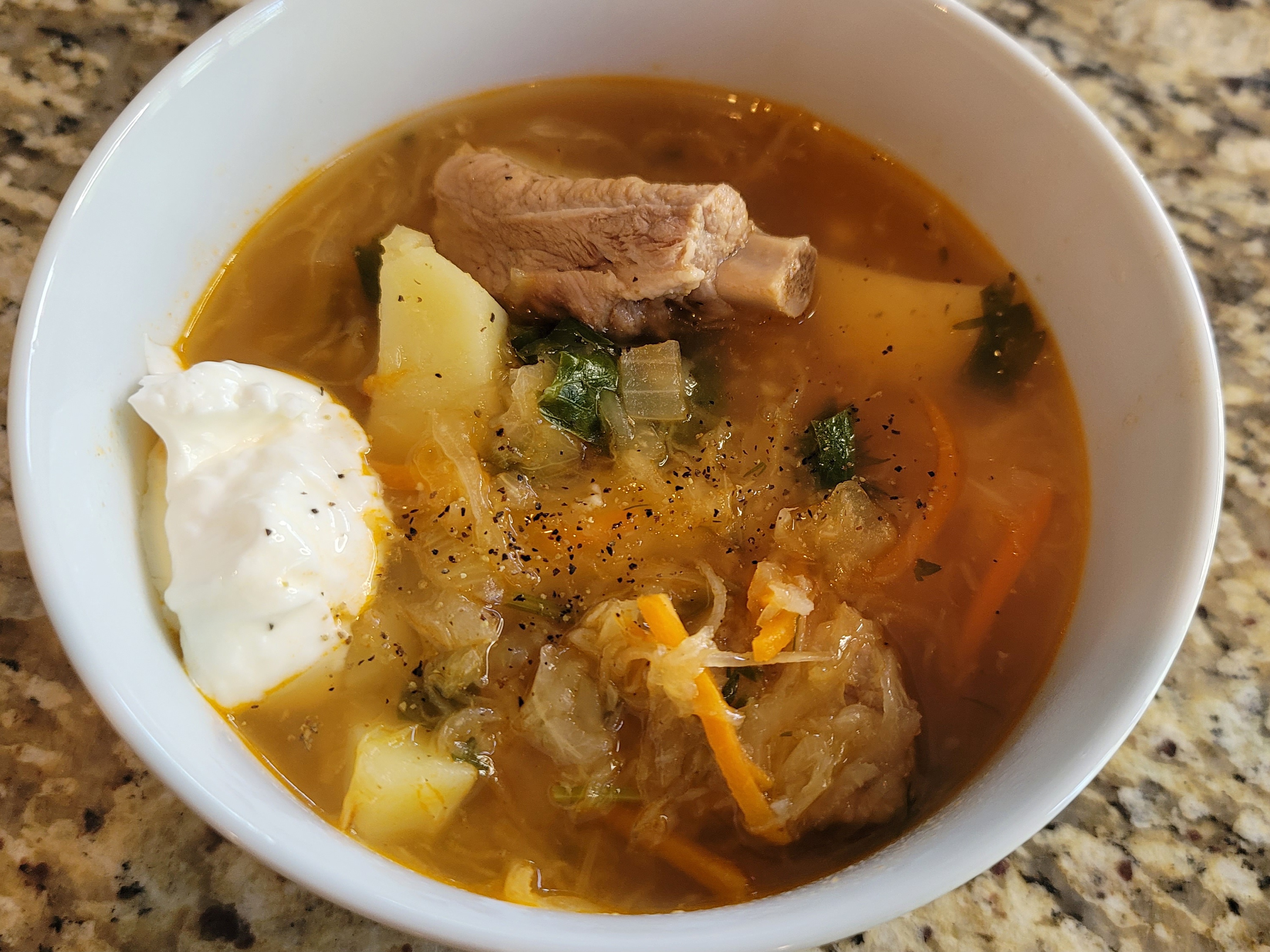 Bowl of traditional Russian sour shchi soup with tender pork ribs, sauerkraut, potatoes, and fresh herbs garnish