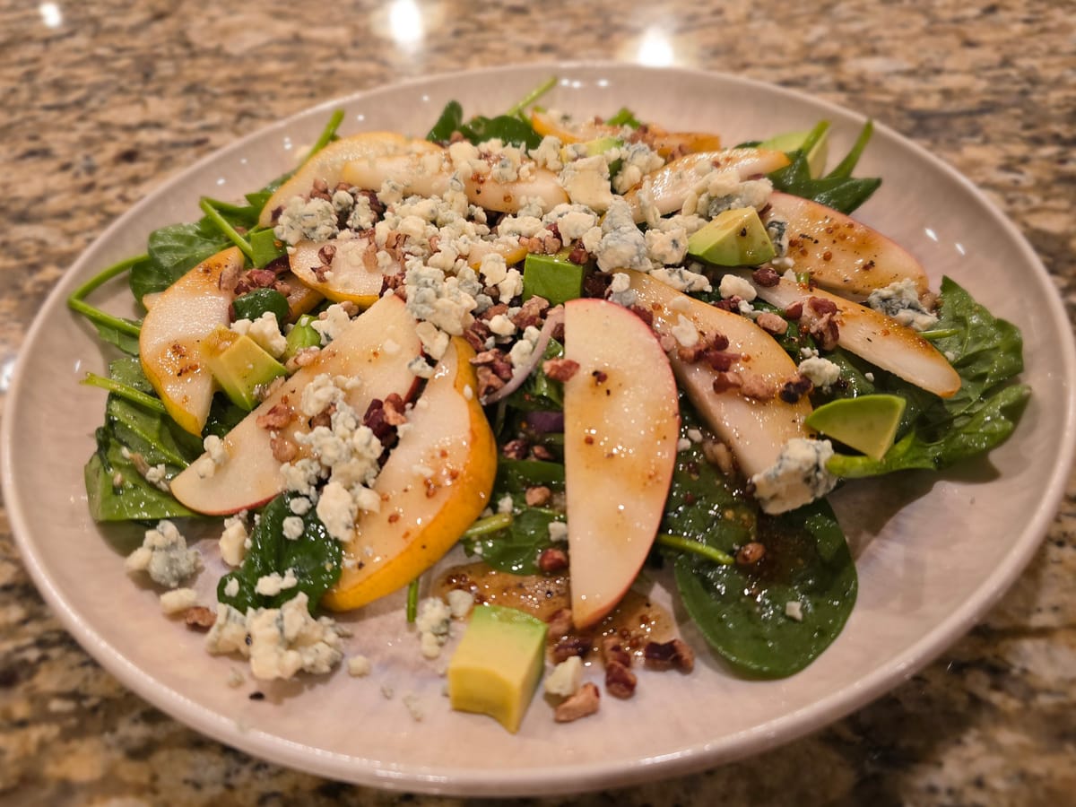 Vibrant spinach, pear and blue cheese salad with walnuts and avocado on a white plate