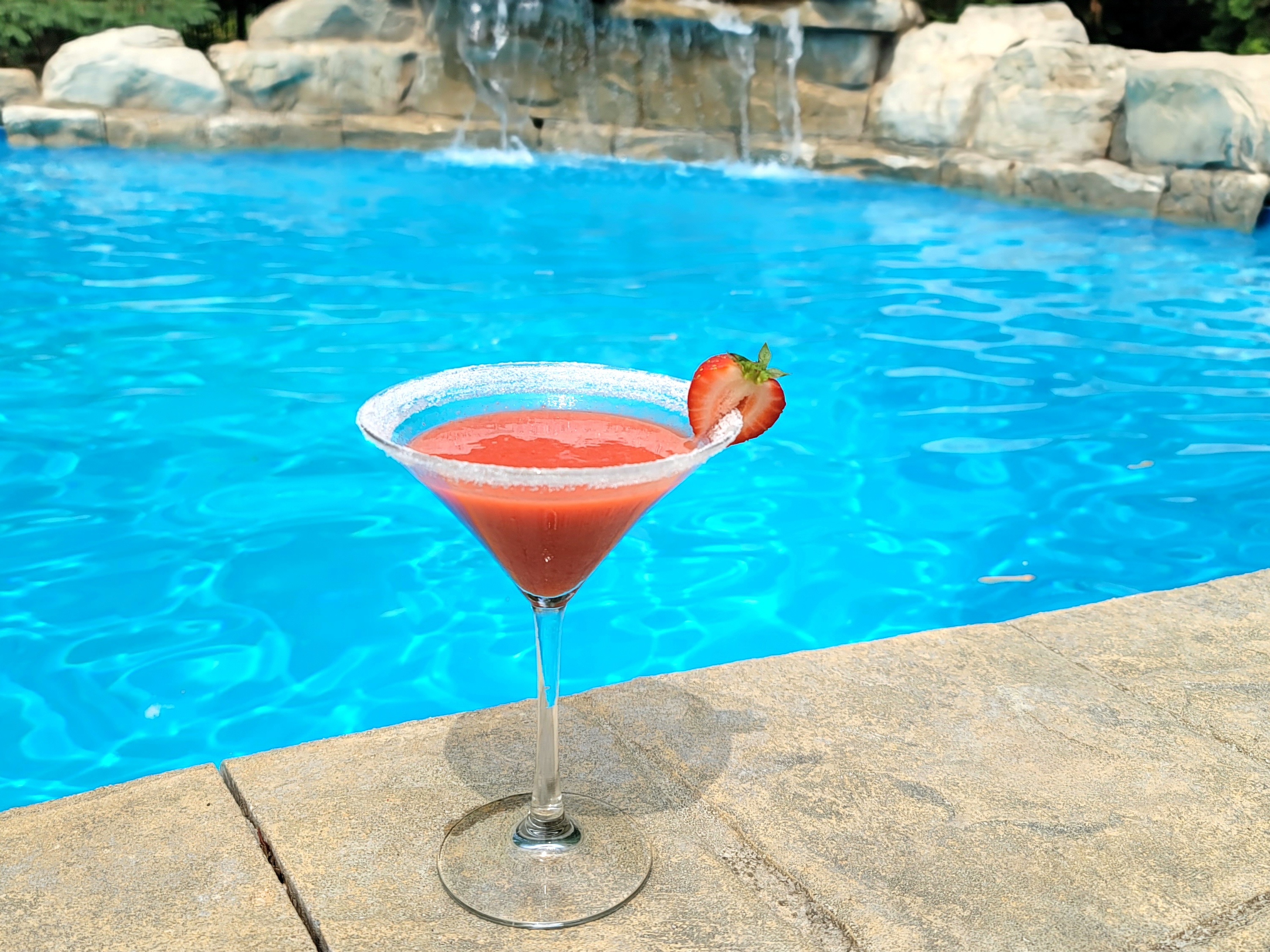 Bright pink frozen strawberry daiquiri in a chilled glass with fresh strawberry garnish and lime wheel
