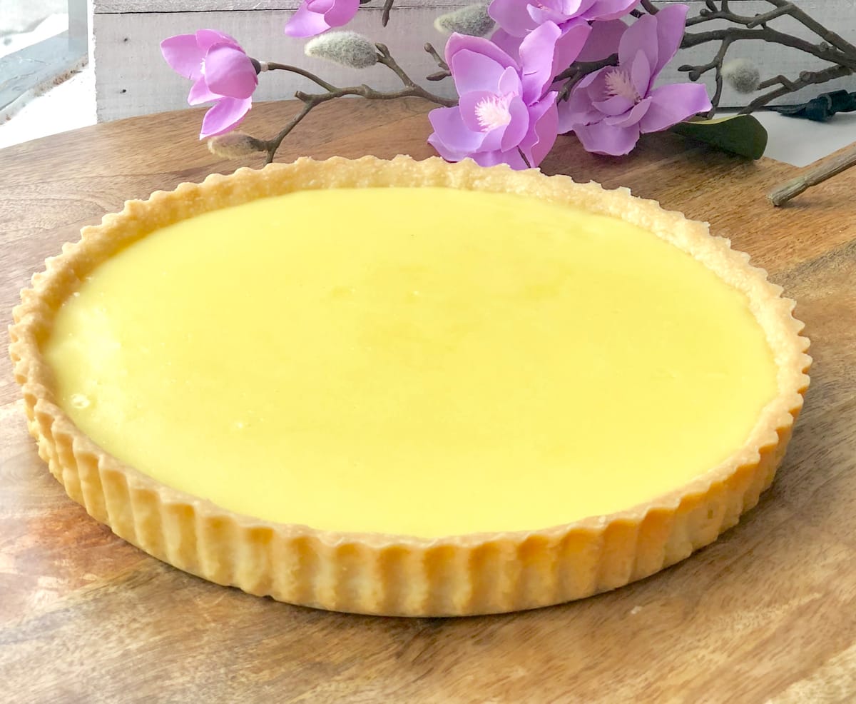 Golden baked tarte au citron with silky lemon filling and crispy pastry crust on a white plate