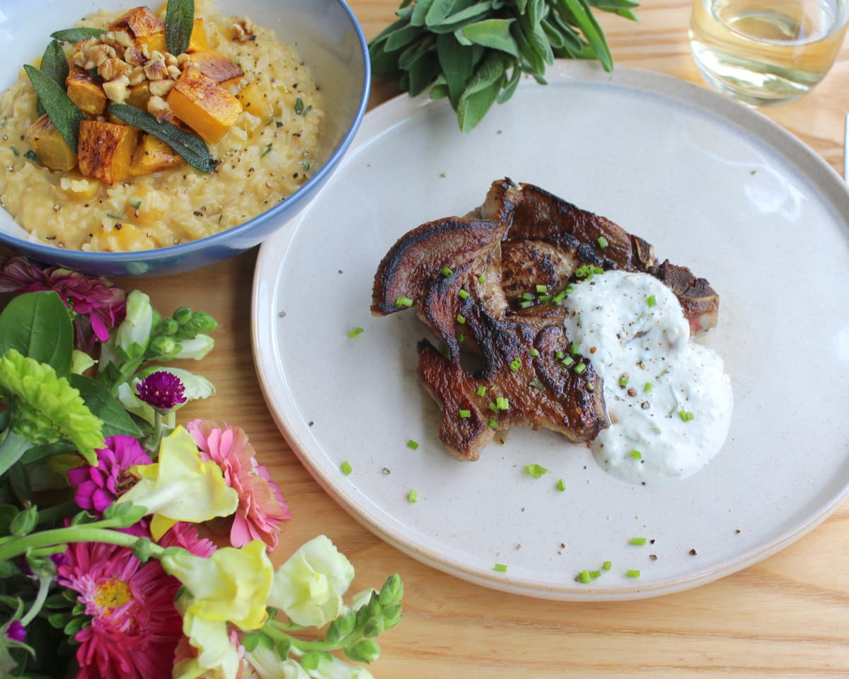 Golden-brown seared thin pork chops on a white plate with herbs and lemon wedges