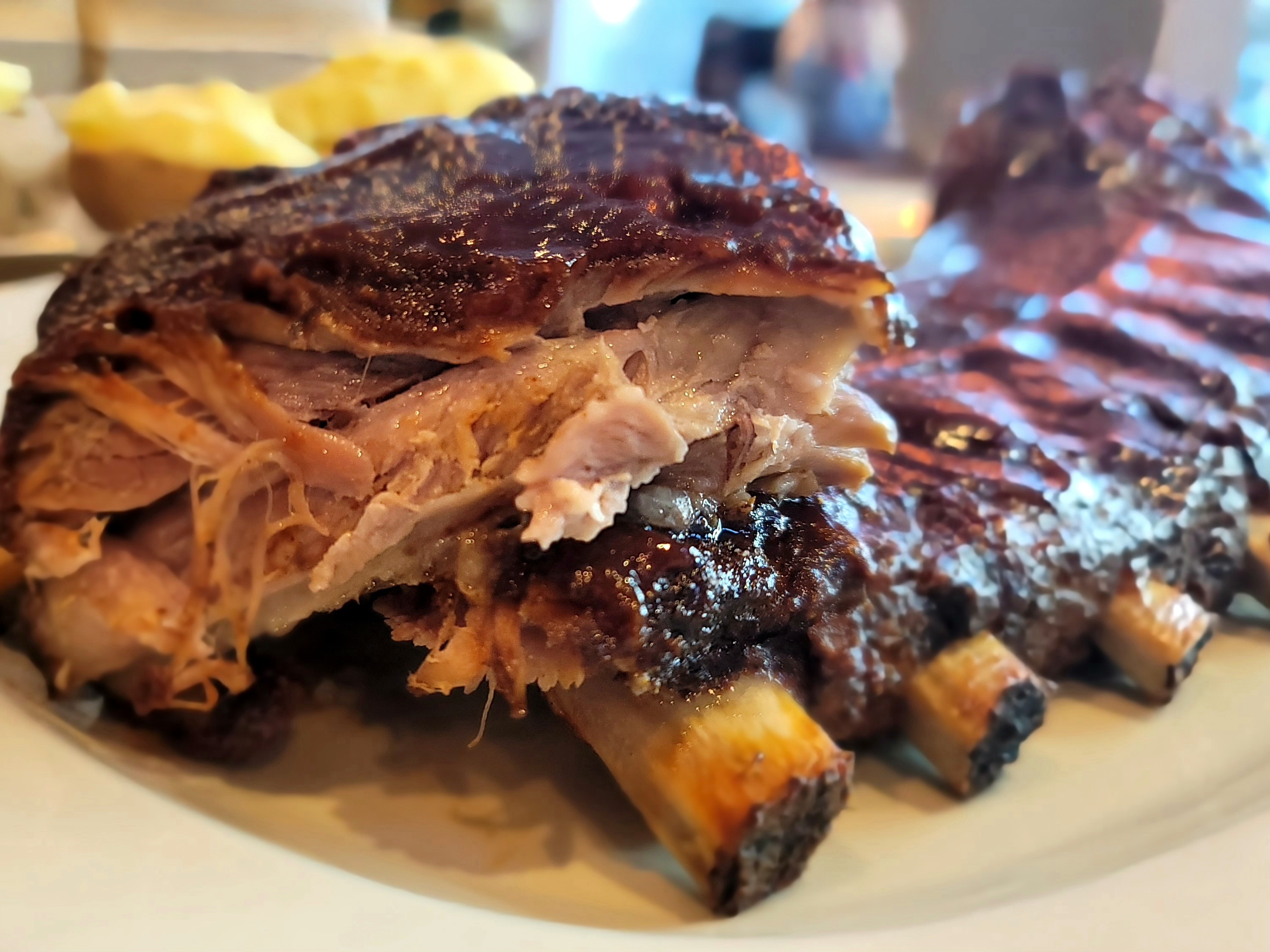 Tender pork ribs glazed with barbecue sauce on a white plate, glistening and fall-apart tender