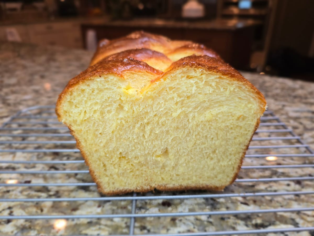 Golden-brown homemade brioche loaf with rich butter-enriched crumb and feathery soft texture on a white surface