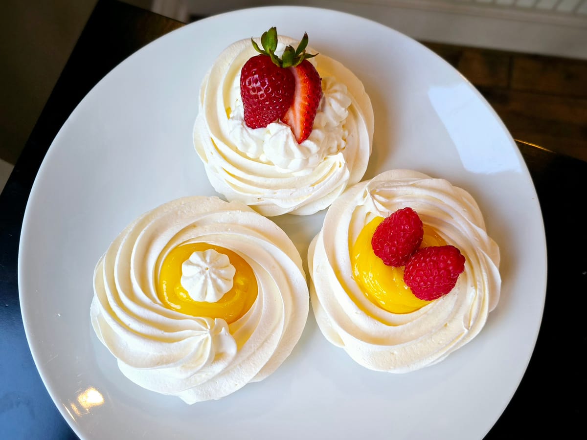 Golden-brown mini pavlovas with crispy meringue shells and marshmallowy centers on a white plate, topped with whipped cream