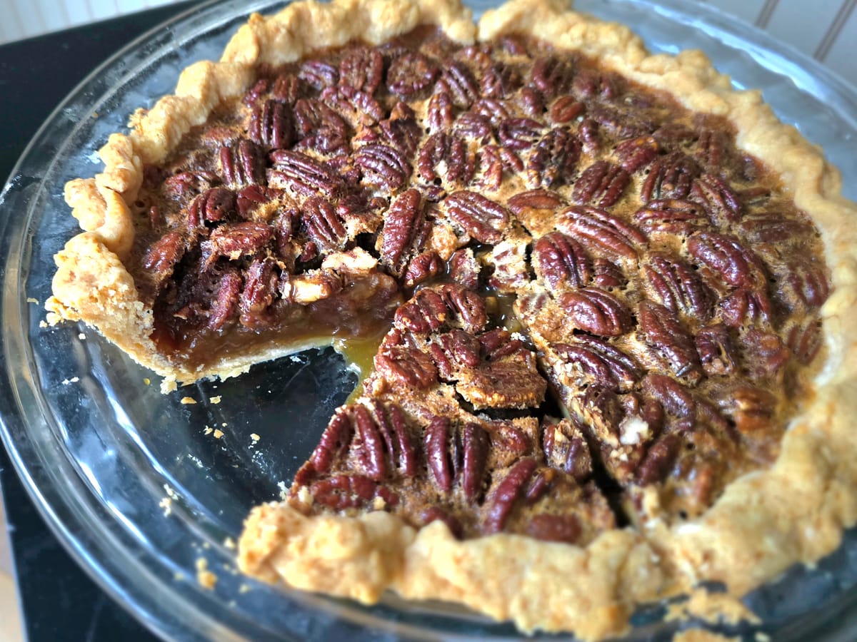 Slice of golden brown pecan pie with caramelized nuts and buttery filling on a white plate