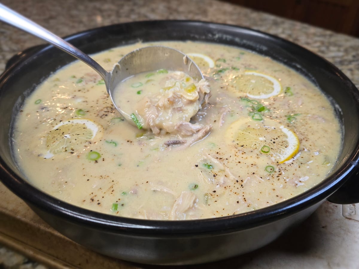 Creamy avgolemono soup with tender chicken, rice, and fresh lemon slices in a white bowl