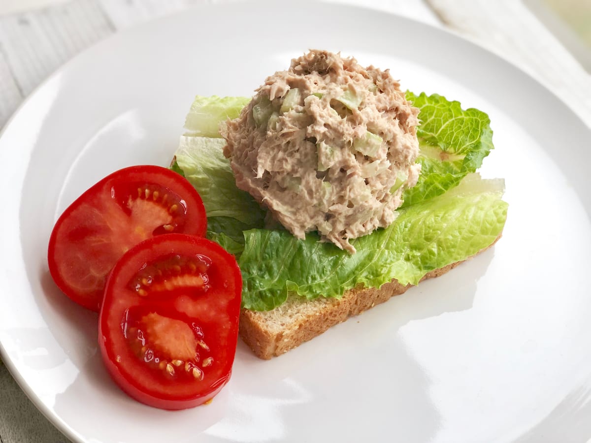 Creamy tuna salad with visible celery, capers, and dill in a white bowl with fresh lemon wedge