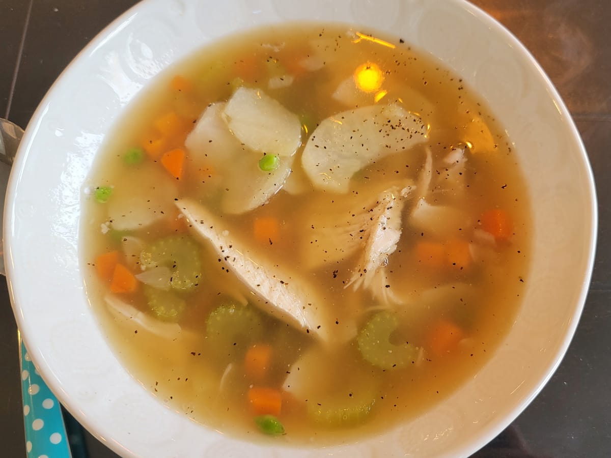 Steaming bowl of turkey soup with shredded turkey, potatoes, and colorful vegetables in a creamy broth
