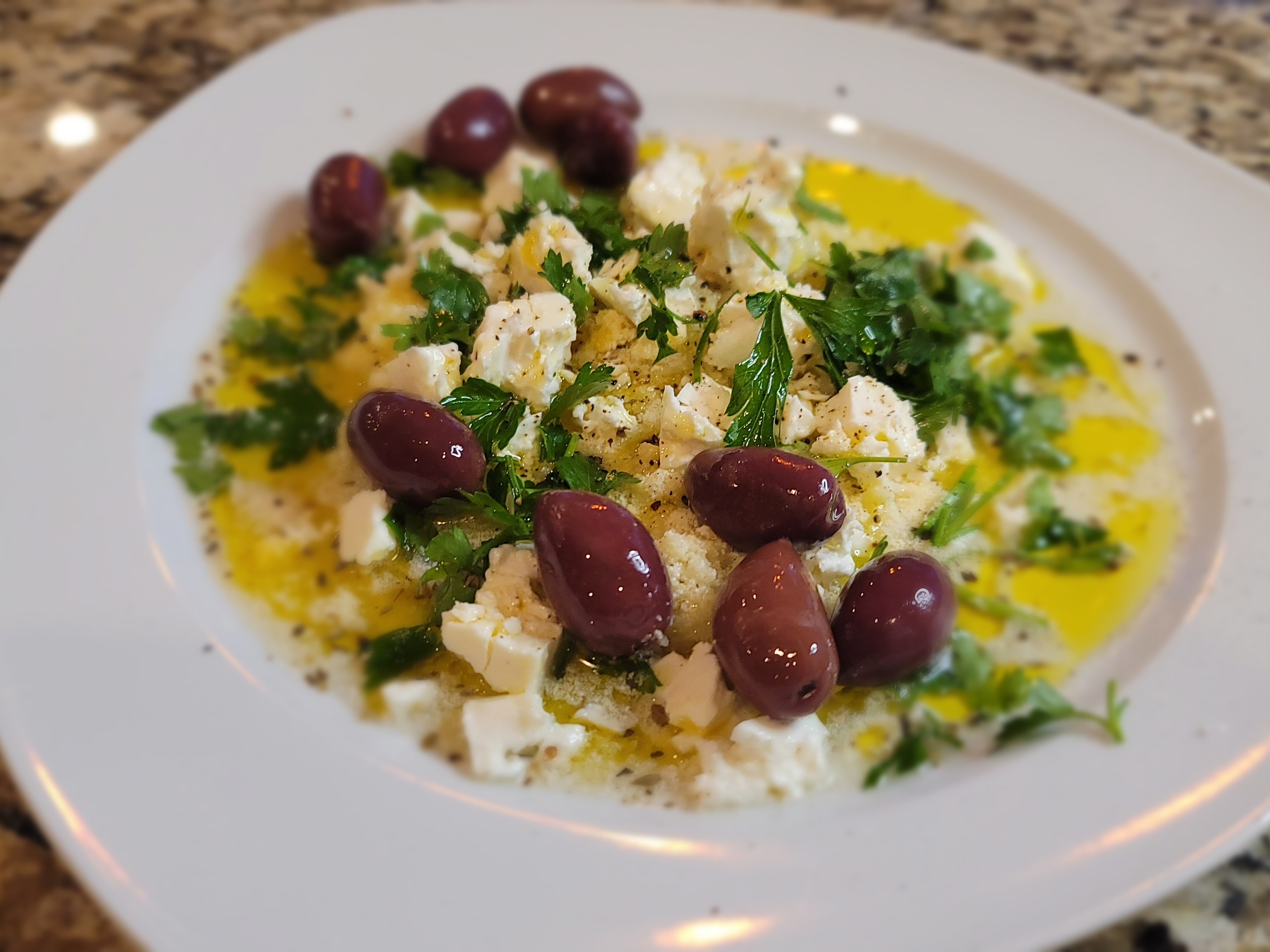 Zesty bread dip with crumbled feta, olives, and fresh parsley in a white bowl with olive oil drizzle