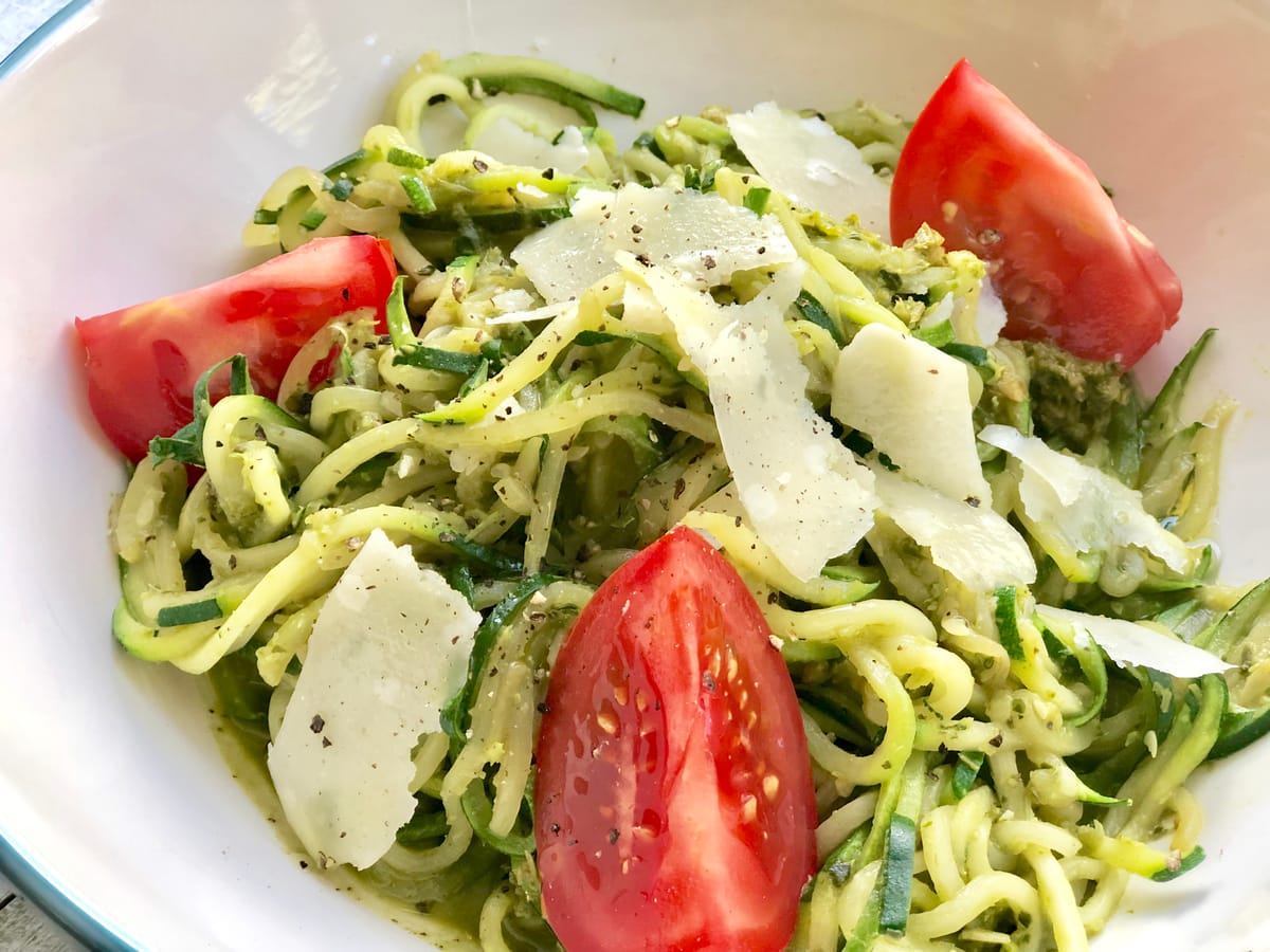 Bright green zucchini noodles coated in vibrant arugula pesto on a white plate, garnished with fresh herbs