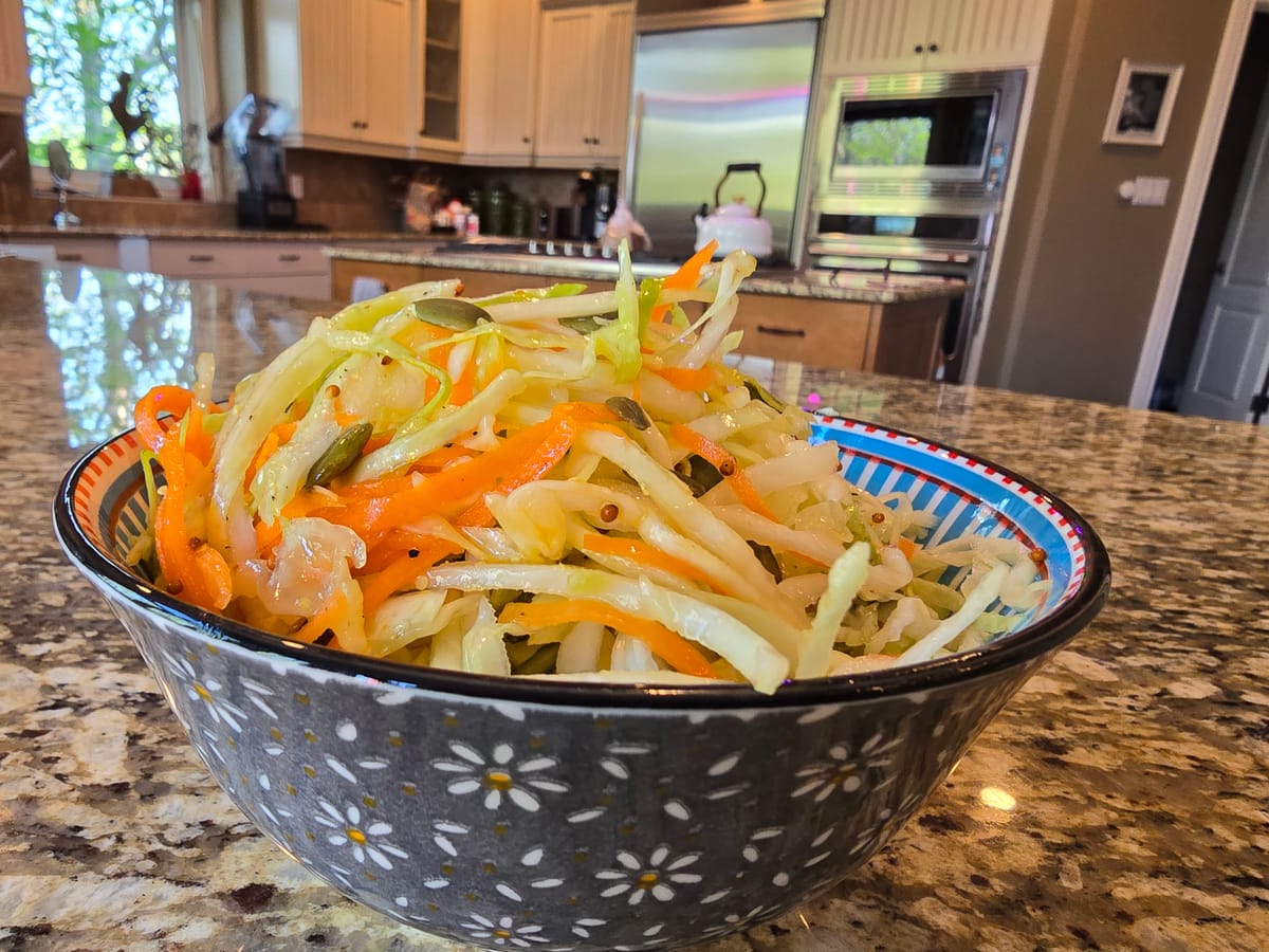 Crisp cabbage and pumpkin seed slaw with maple Dijon vinaigrette on a white plate, garnished with fresh herbs and green vegetables