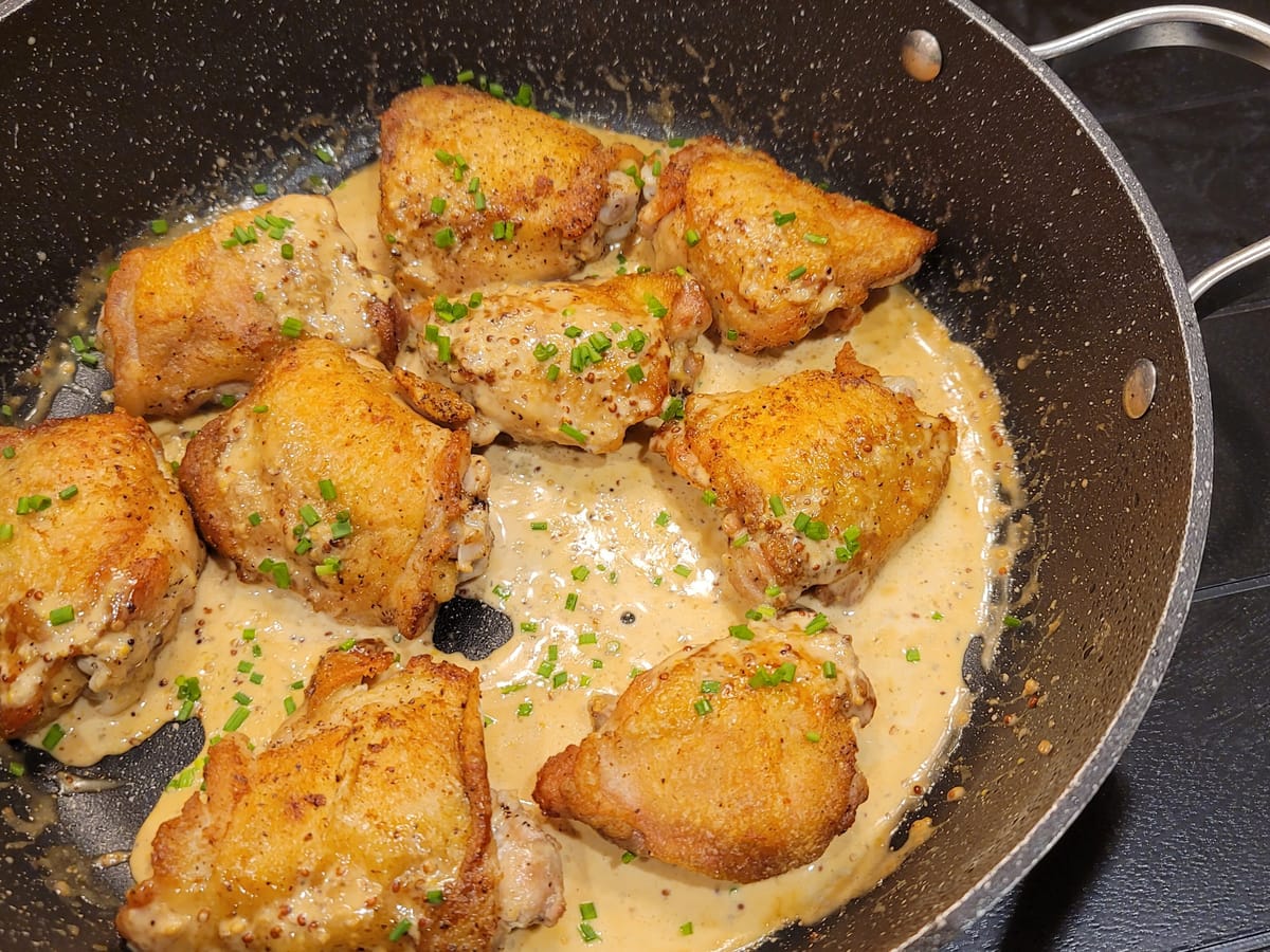 Golden crispy-skinned chicken thighs in creamy mustard sauce on a white plate with fresh herbs garnish