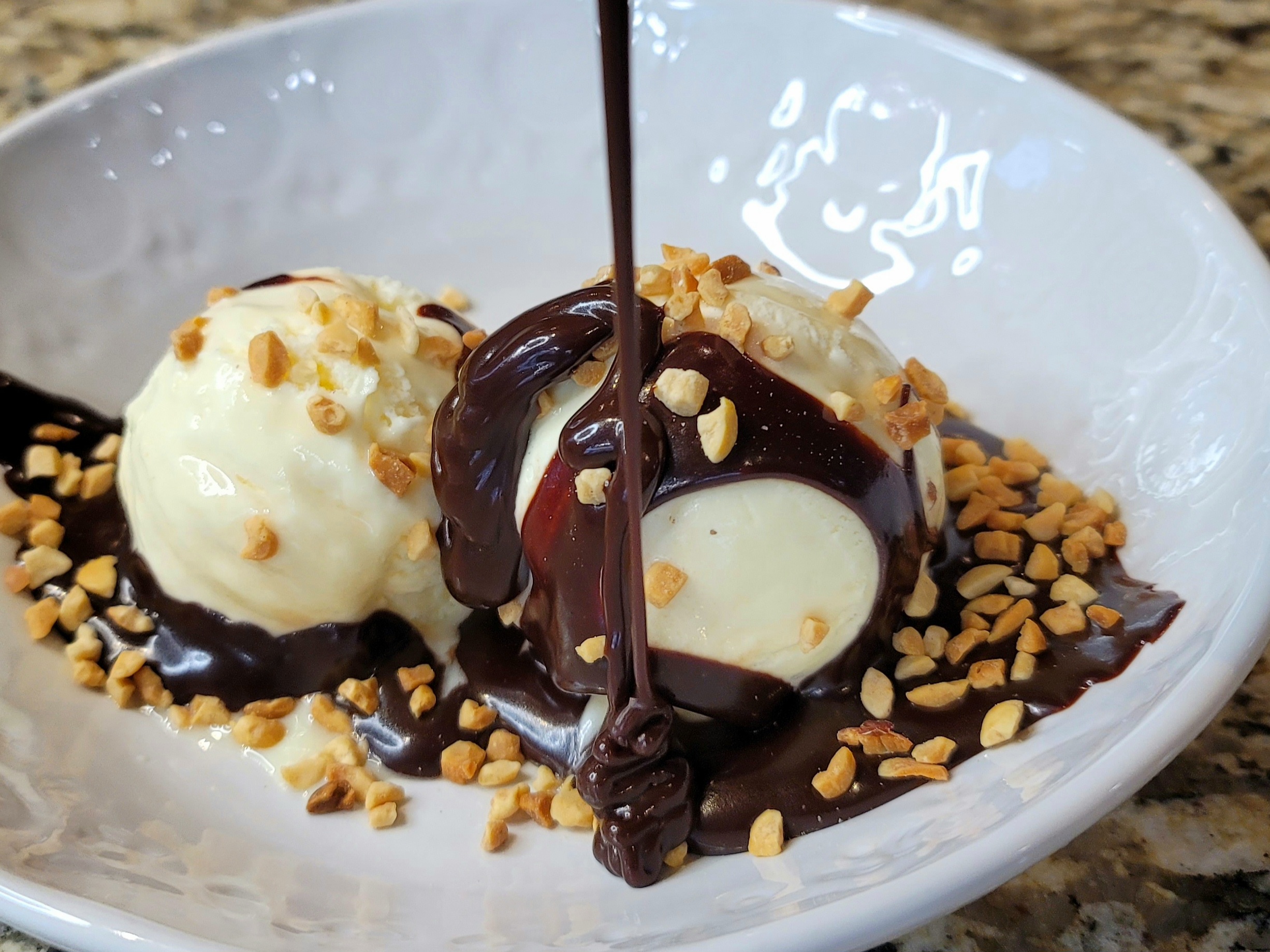 Rich, glossy hot fudge sauce dripping over vanilla ice cream with chocolate pieces