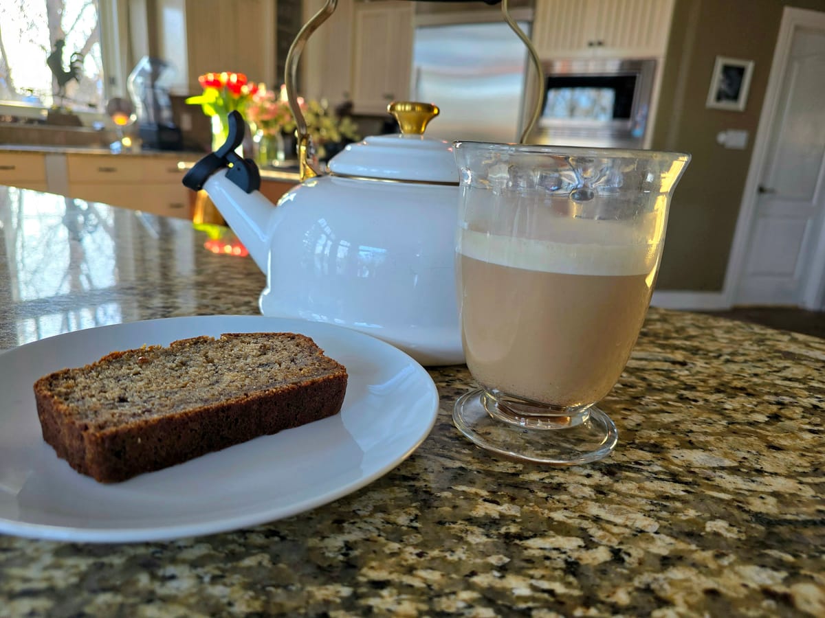 Creamy snickerdoodle latte in a white mug topped with cinnamon sugar, steam rising, with coffee beans nearby