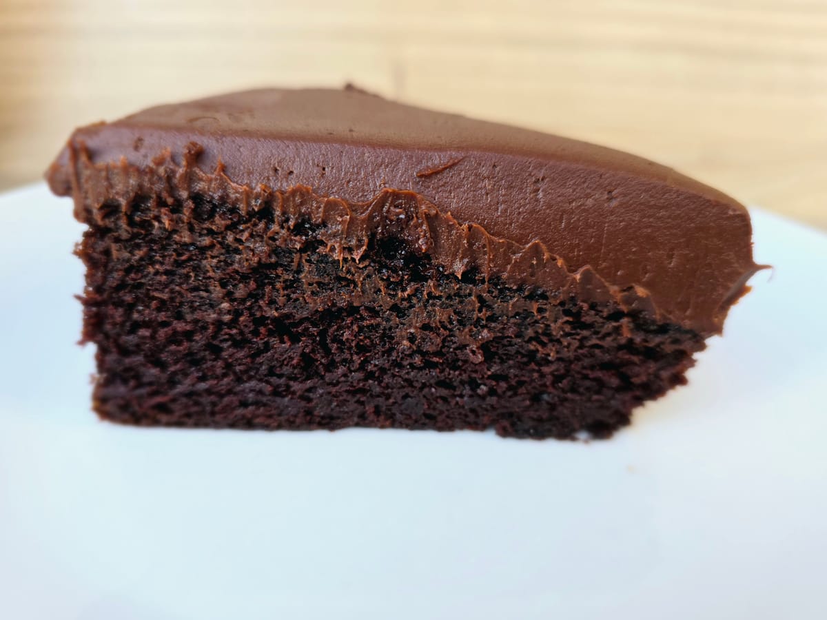 Slice of rich chocolate cake with creamy sour cream frosting on a white plate, showcasing the moist, tender crumb