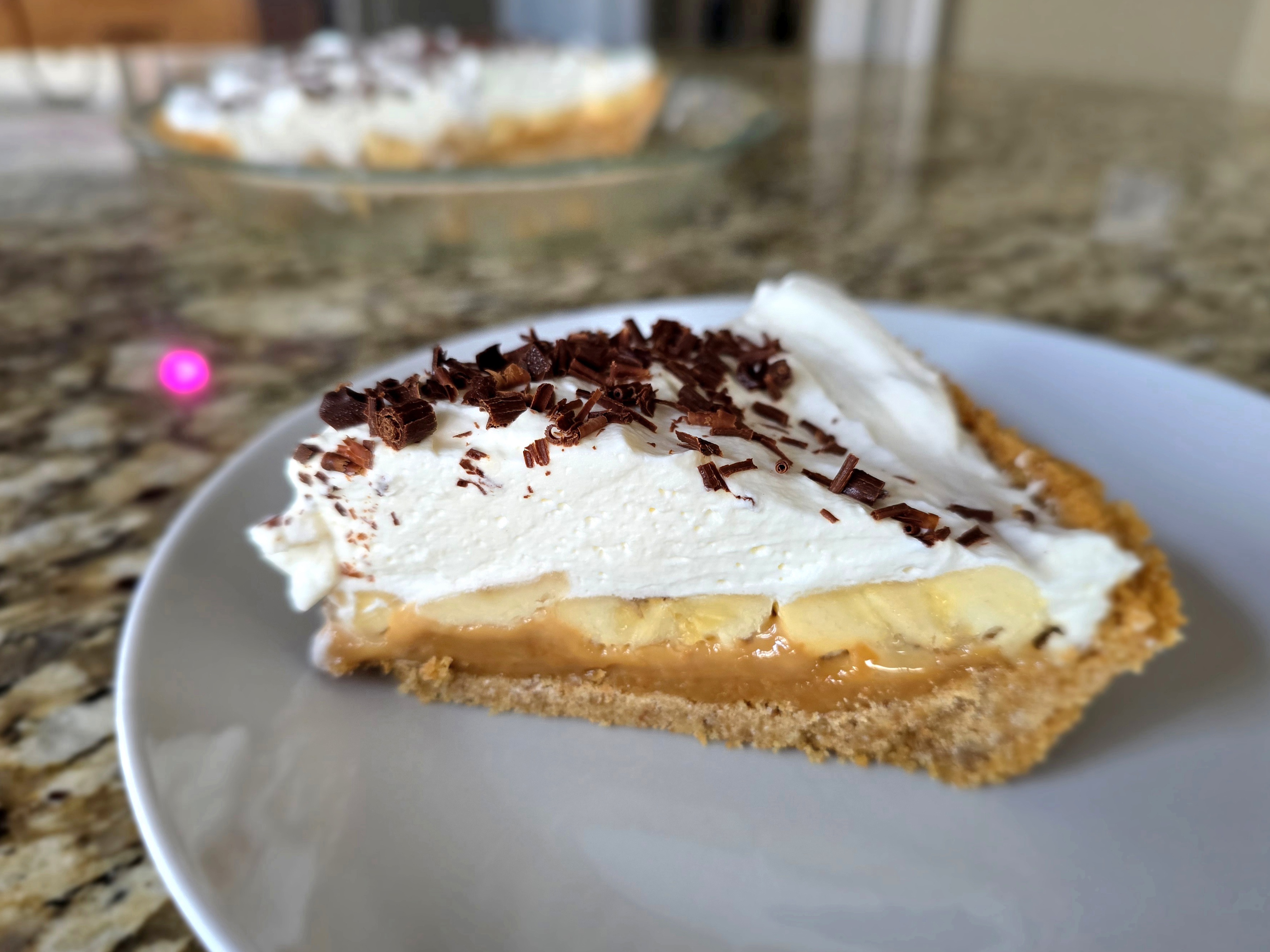 Banoffee pie with layers of graham cracker crust, caramel dulce de leche, sliced bananas, and whipped cream topping on a white plate