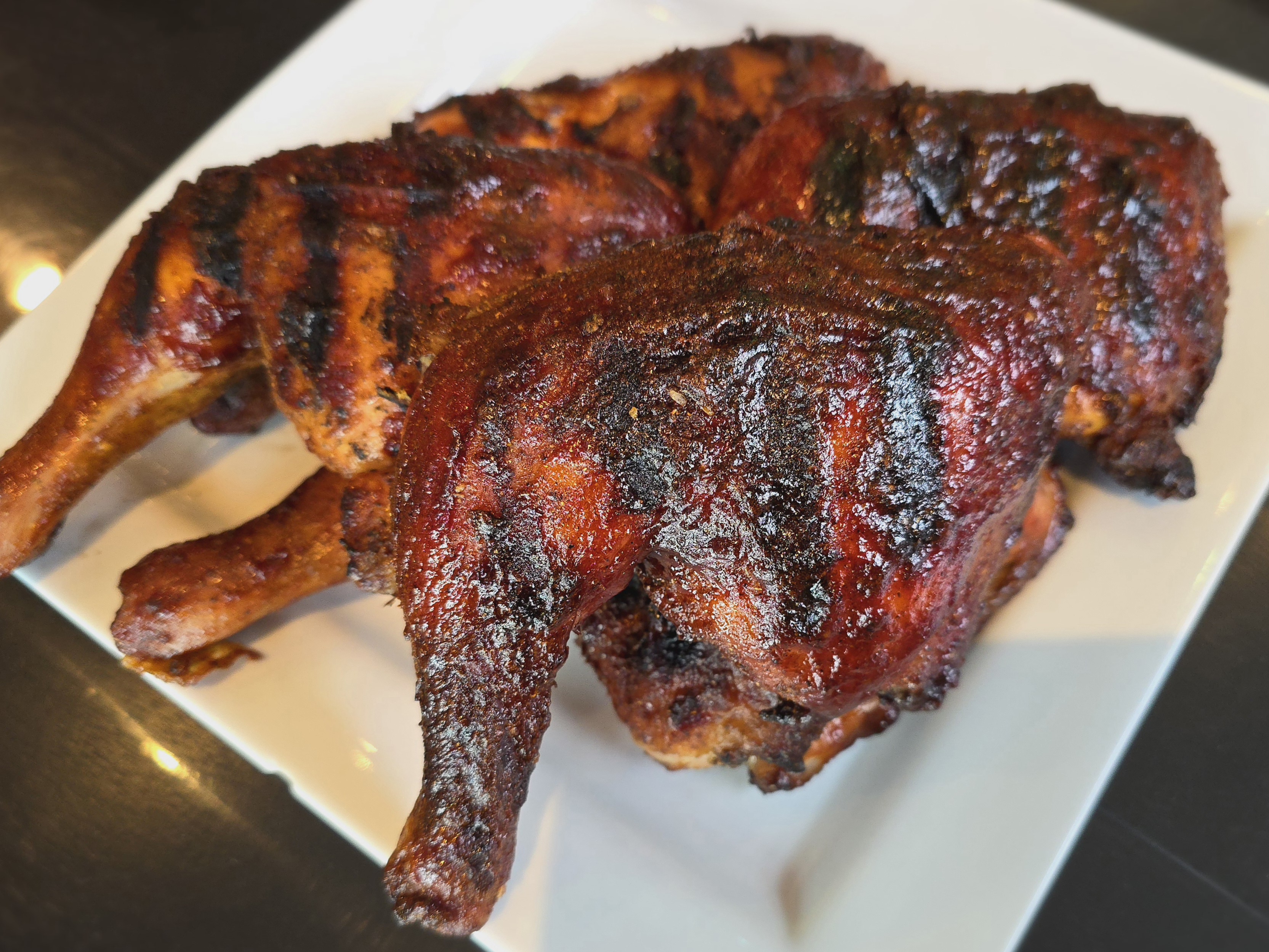 Golden-brown barbecue chicken legs on a white plate with charred edges and glossy BBQ sauce