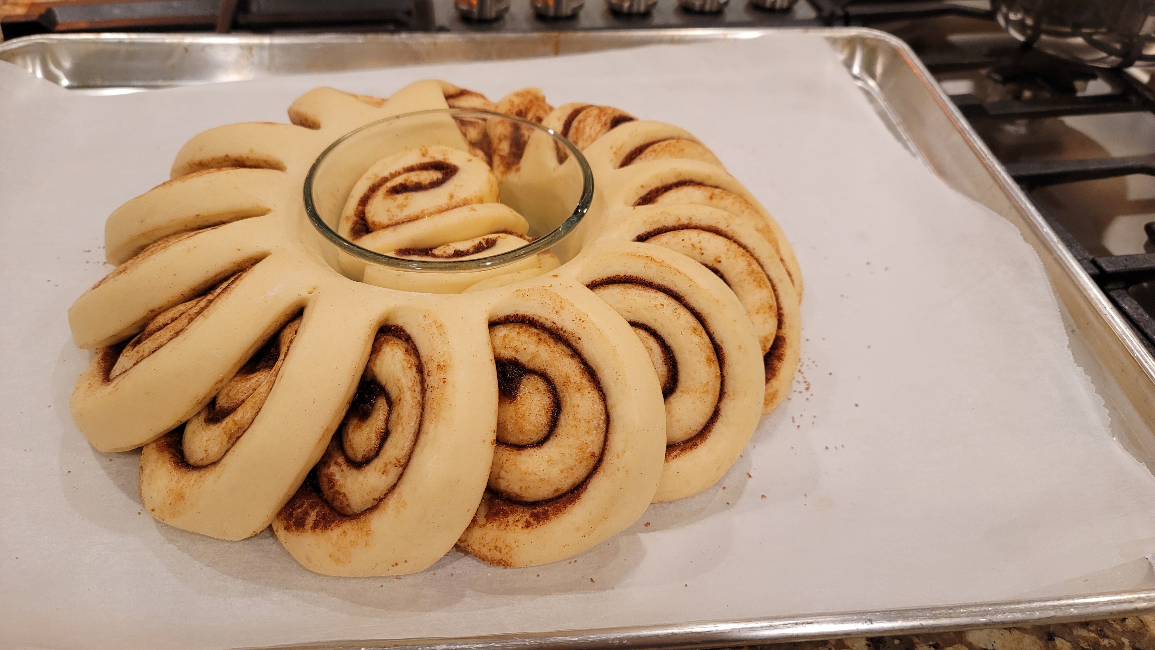 Golden-brown cinnamon bun wreath arranged in a circle on a white plate with white icing drizzle and cinnamon swirls visible