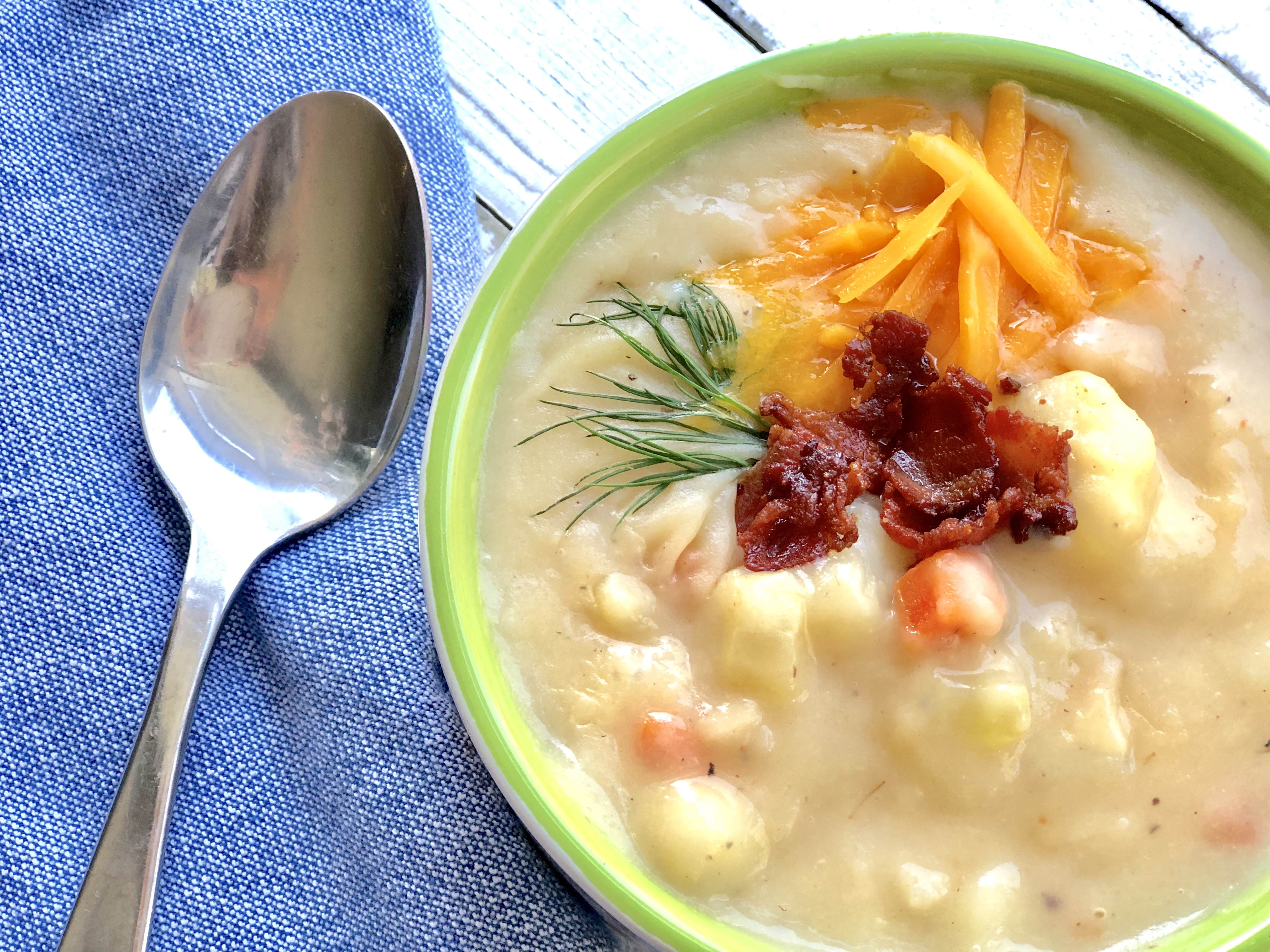 Creamy potato bacon soup with crispy bacon bits and fresh herbs in a white bowl on a rustic table